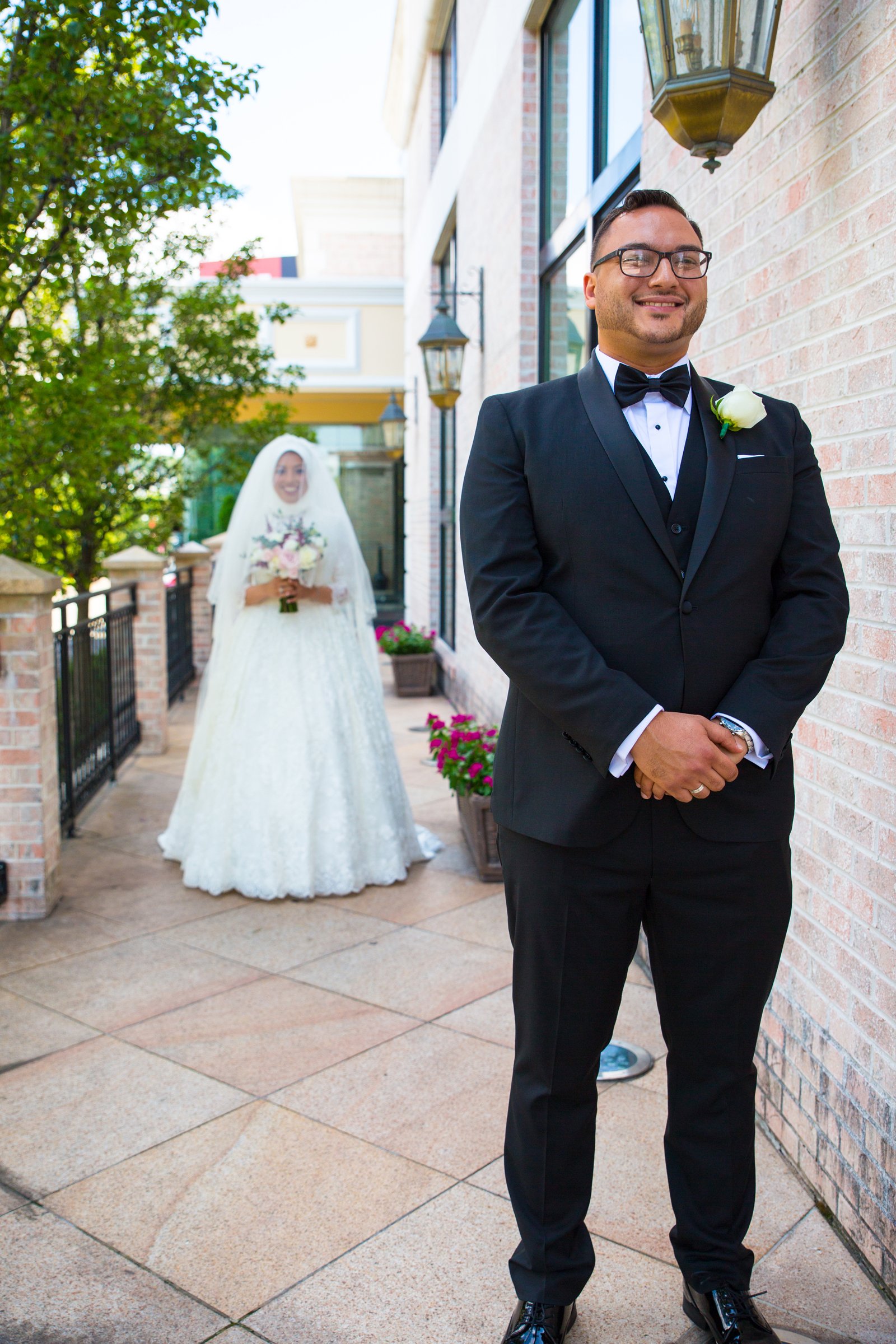 Bride and groom during a wedding first look, outdoors with greenery and brick building in background.