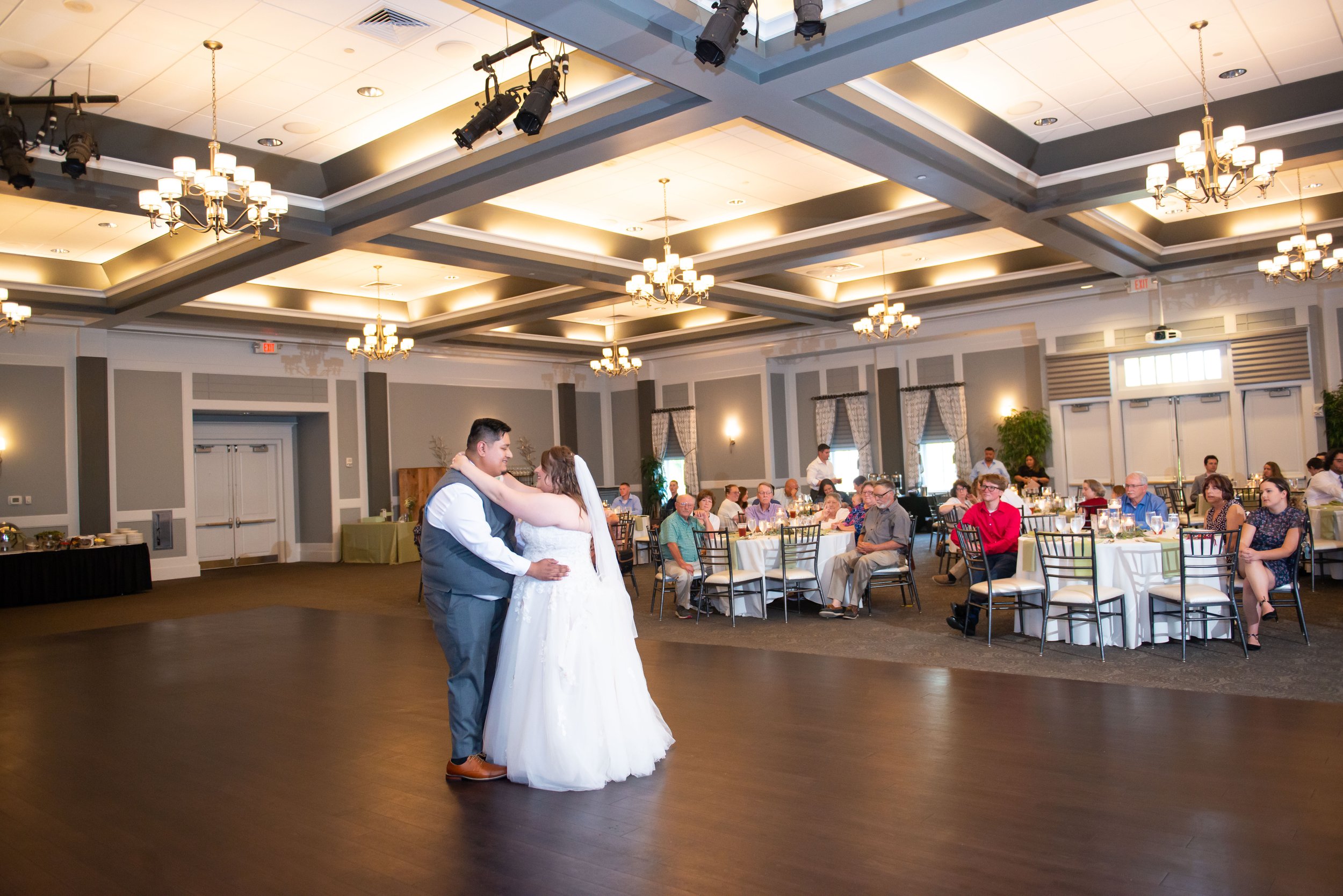 A couple dancing in a decorated banquet hall with guests seated at tables watching.