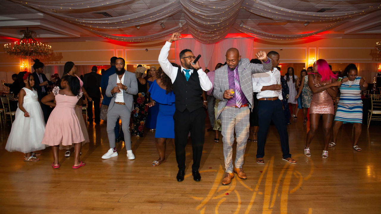 People dancing at a lively party in a decorated ballroom with festive lighting.