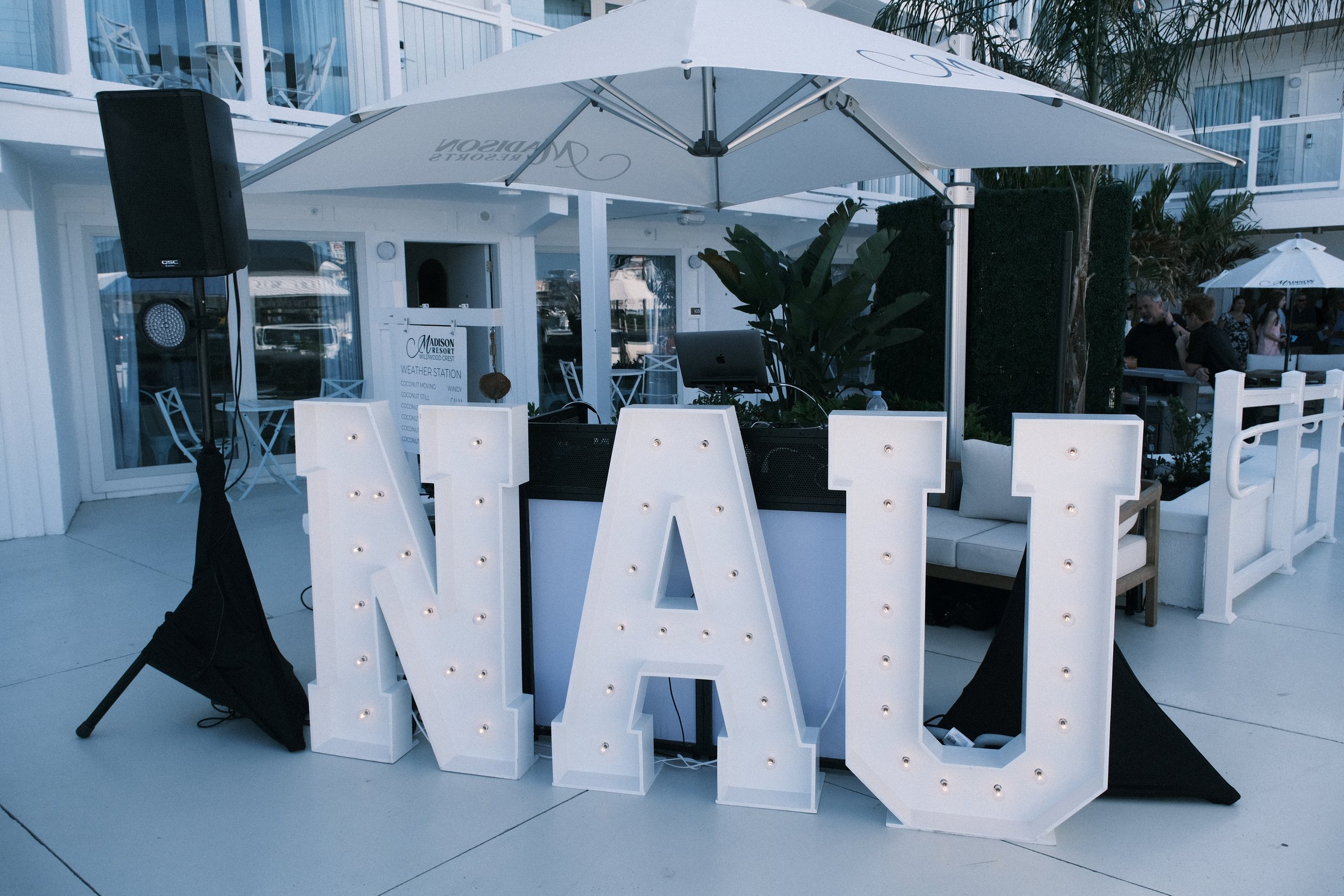 Large illuminated "NAU" sign with light bulbs, outdoor setting with umbrella, and patio furniture.