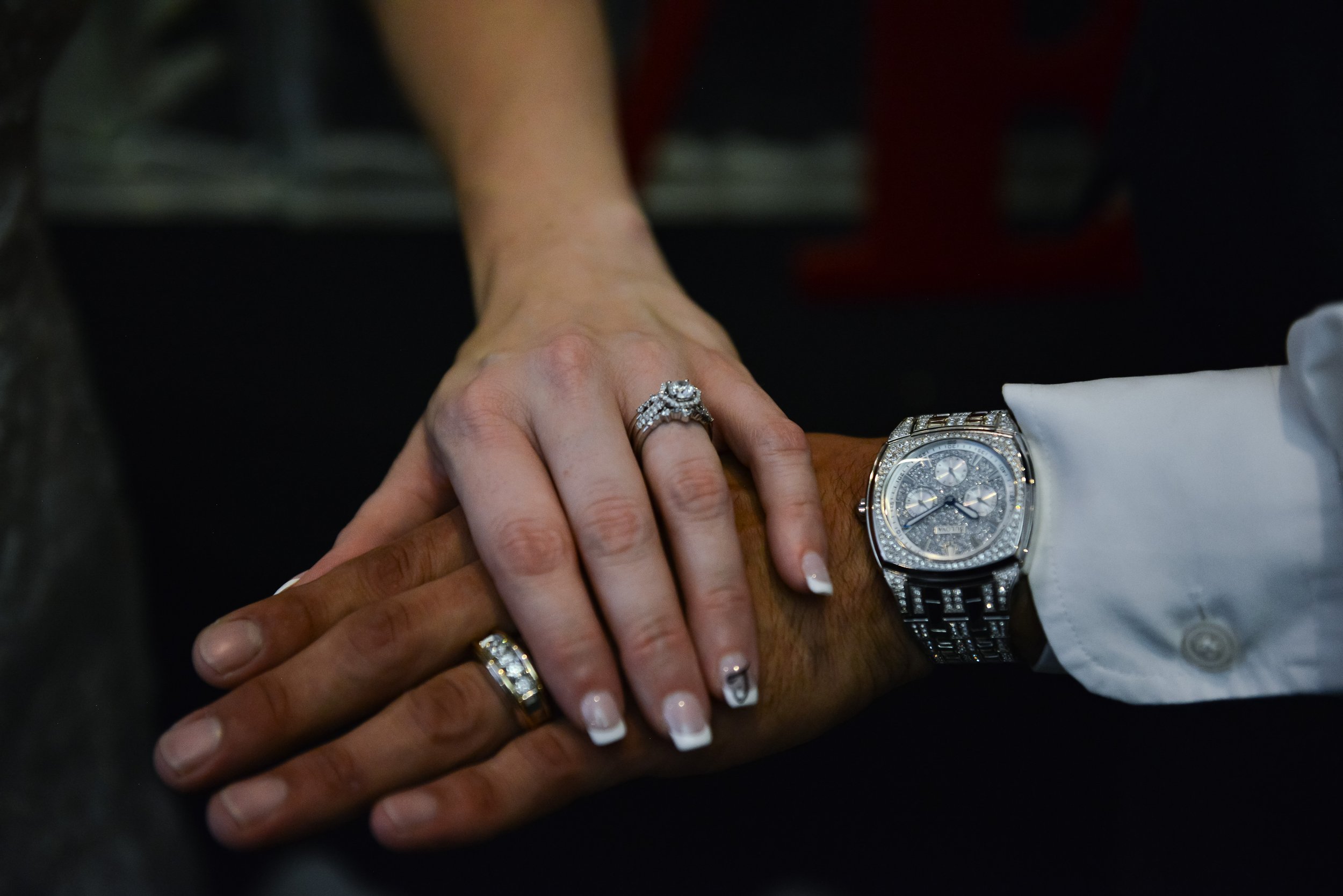 Close-up of two hands with wedding rings and a luxury watch.