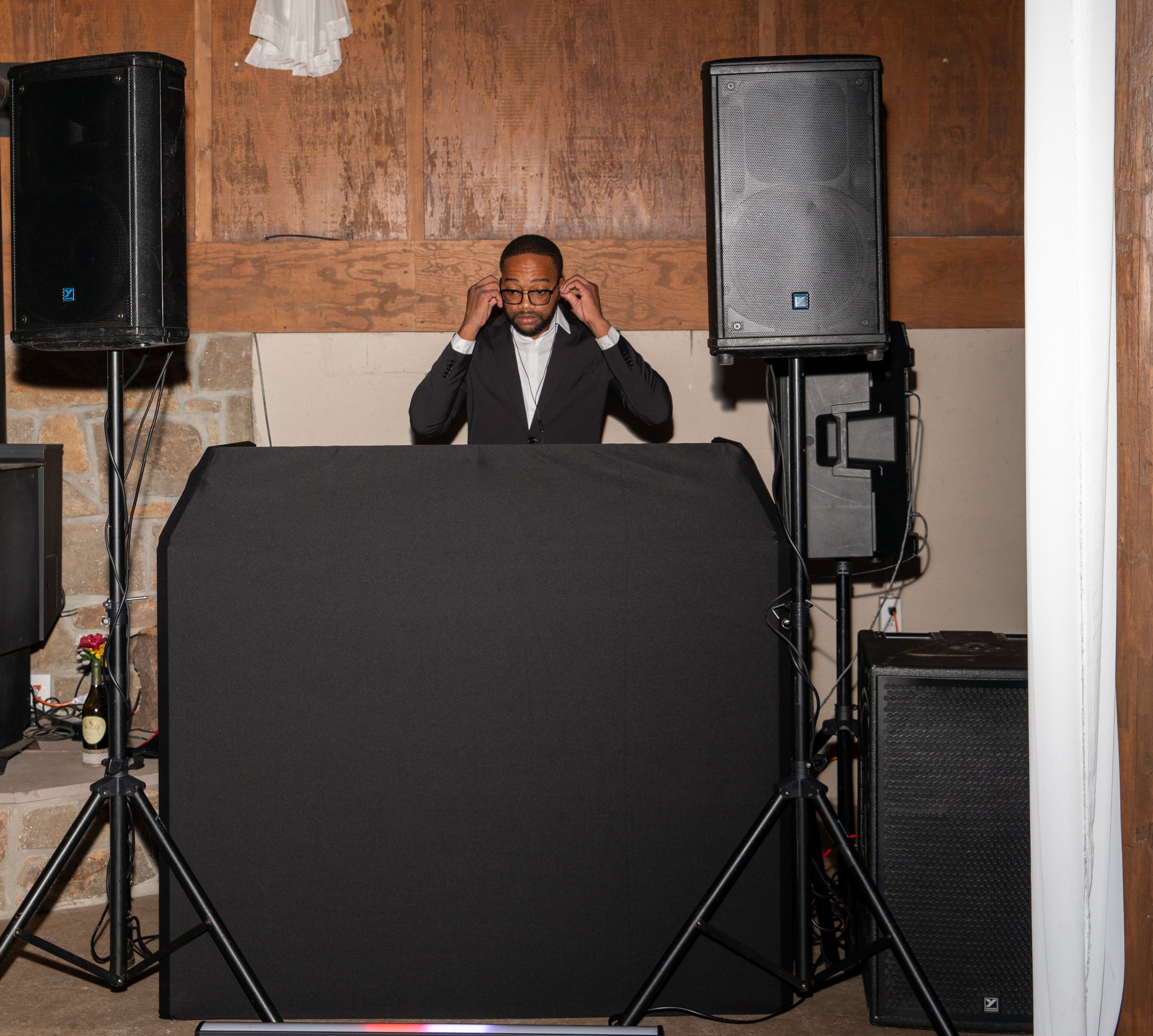 DJ stands behind a covered table with speakers and equipment at an event.