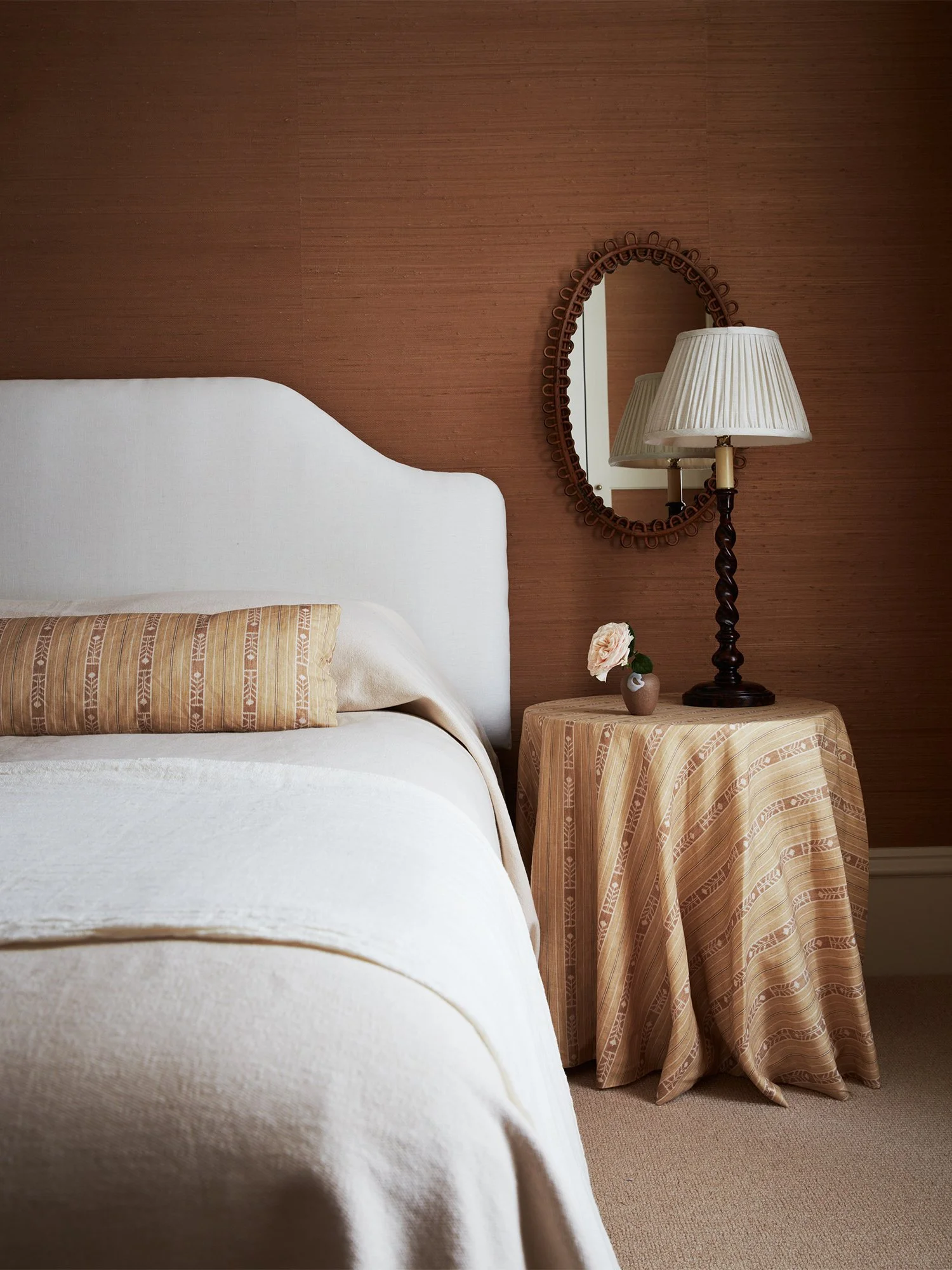 Bedroom closeup of bed and nightstand with mirror, lamp and vase.