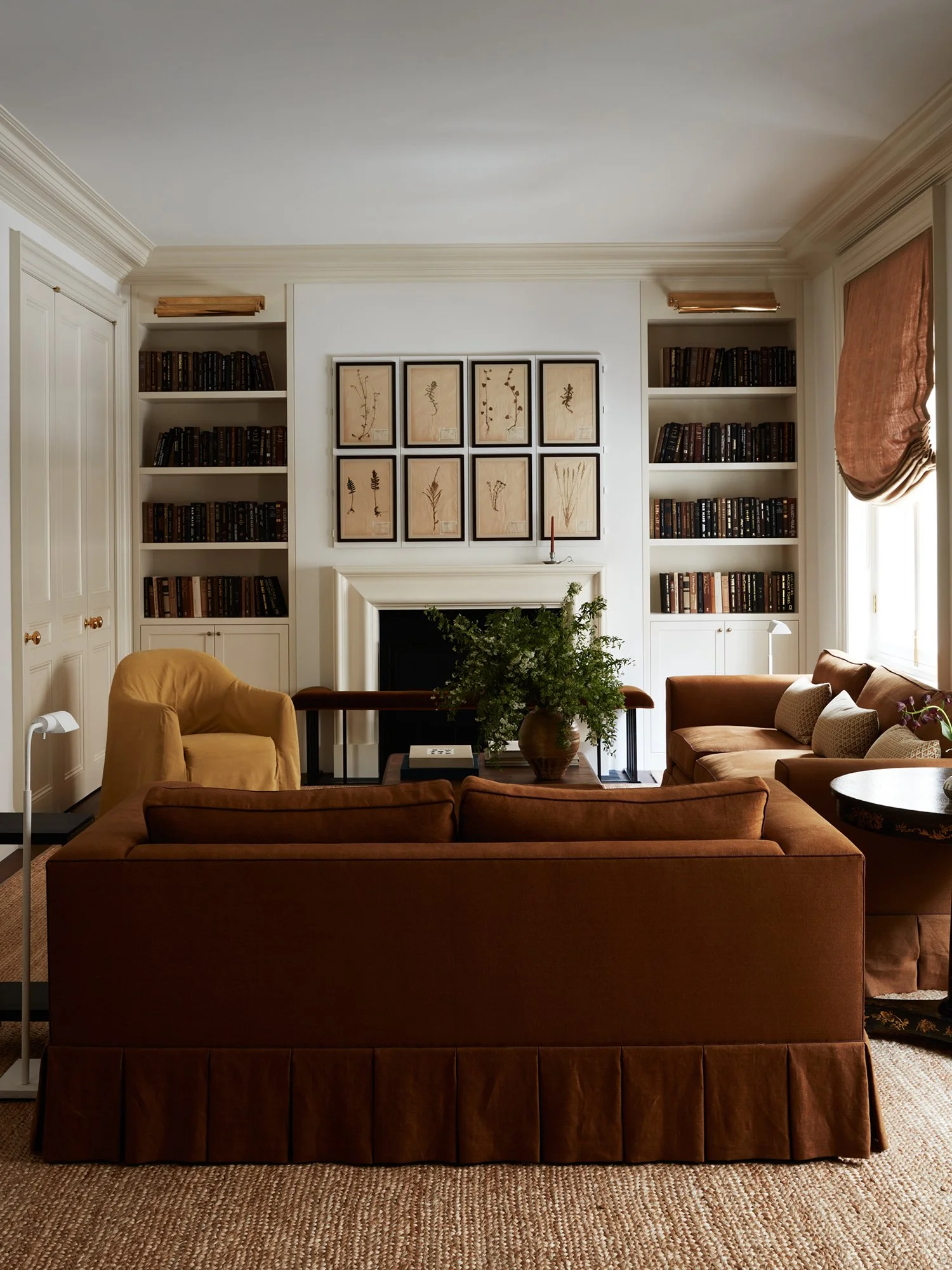 View of living room with two sofas, side chair, side tables, fireplace with bookshelves and art.