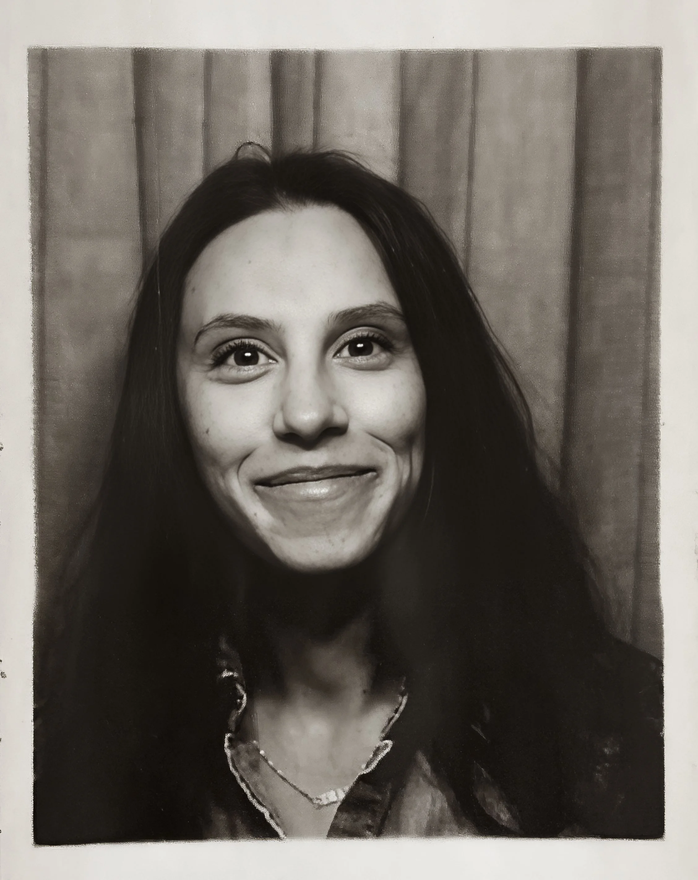 Black and white portrait of a woman with long dark hair, wearing a patterned scarf around her neck and a striped shirt, outdoors, smiling softly.