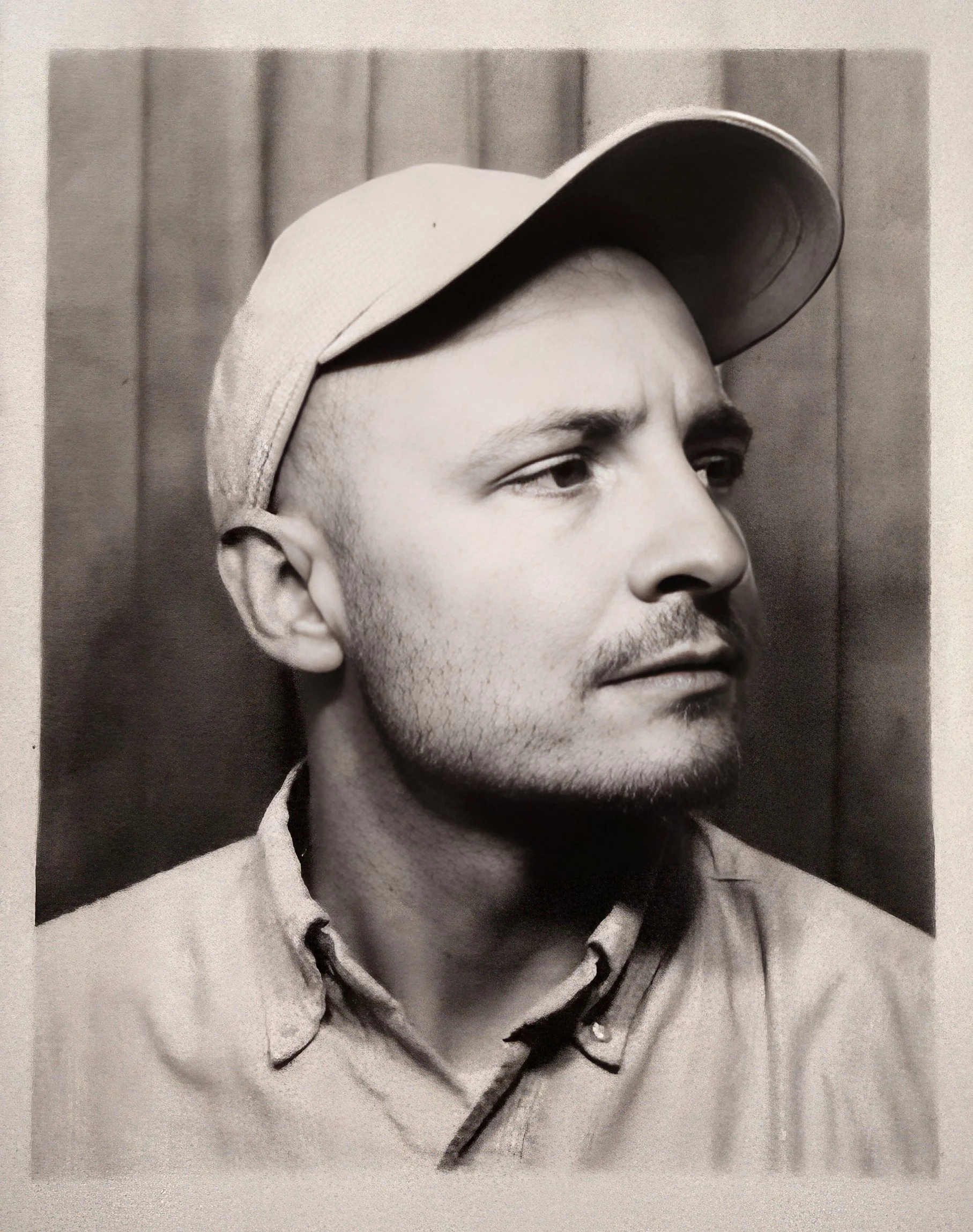 Black and white close-up portrait of a young man wearing a cap outdoors.