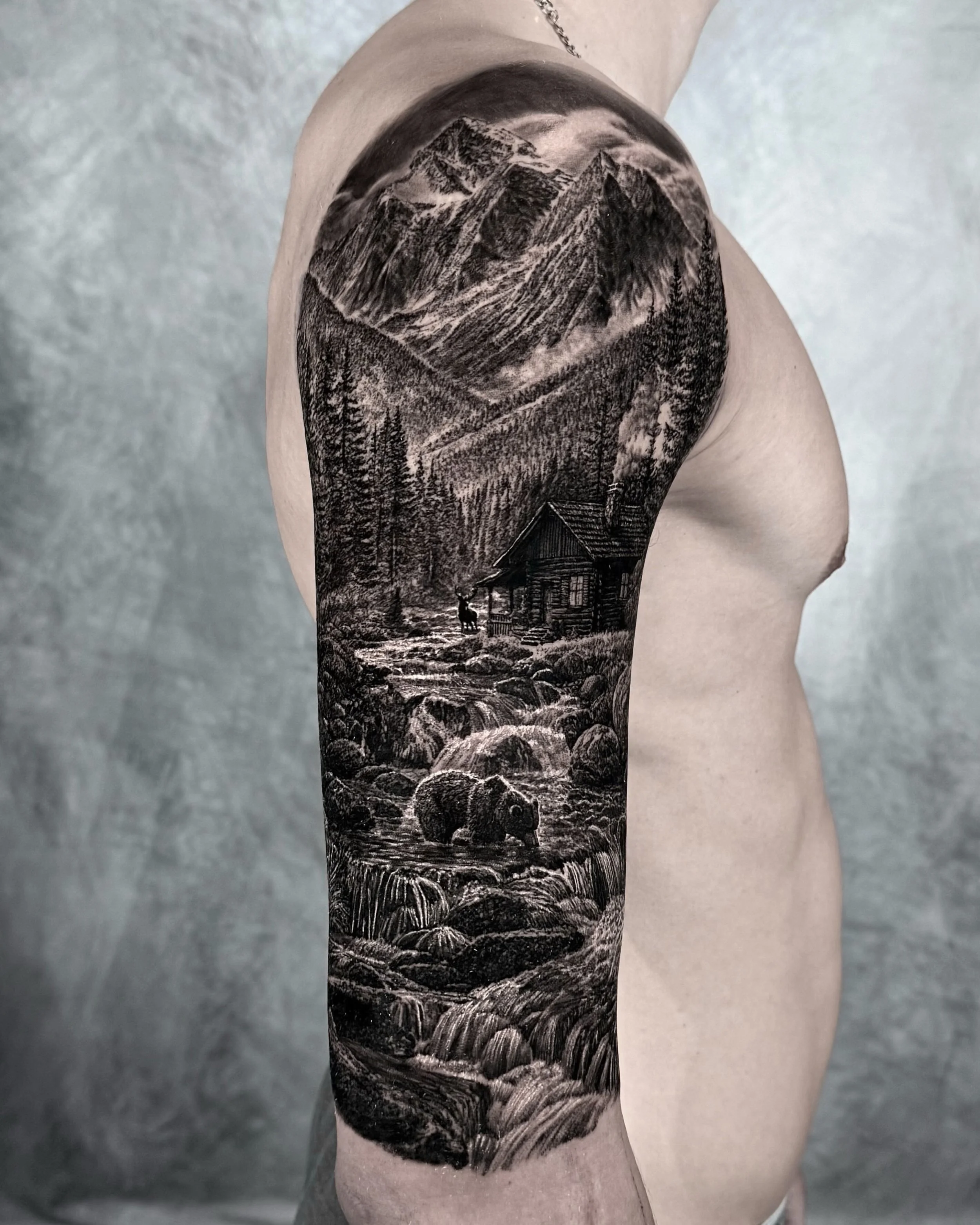 Mountain cabin and bear landscape realism tattoo on the upper arm by Etgar Oak