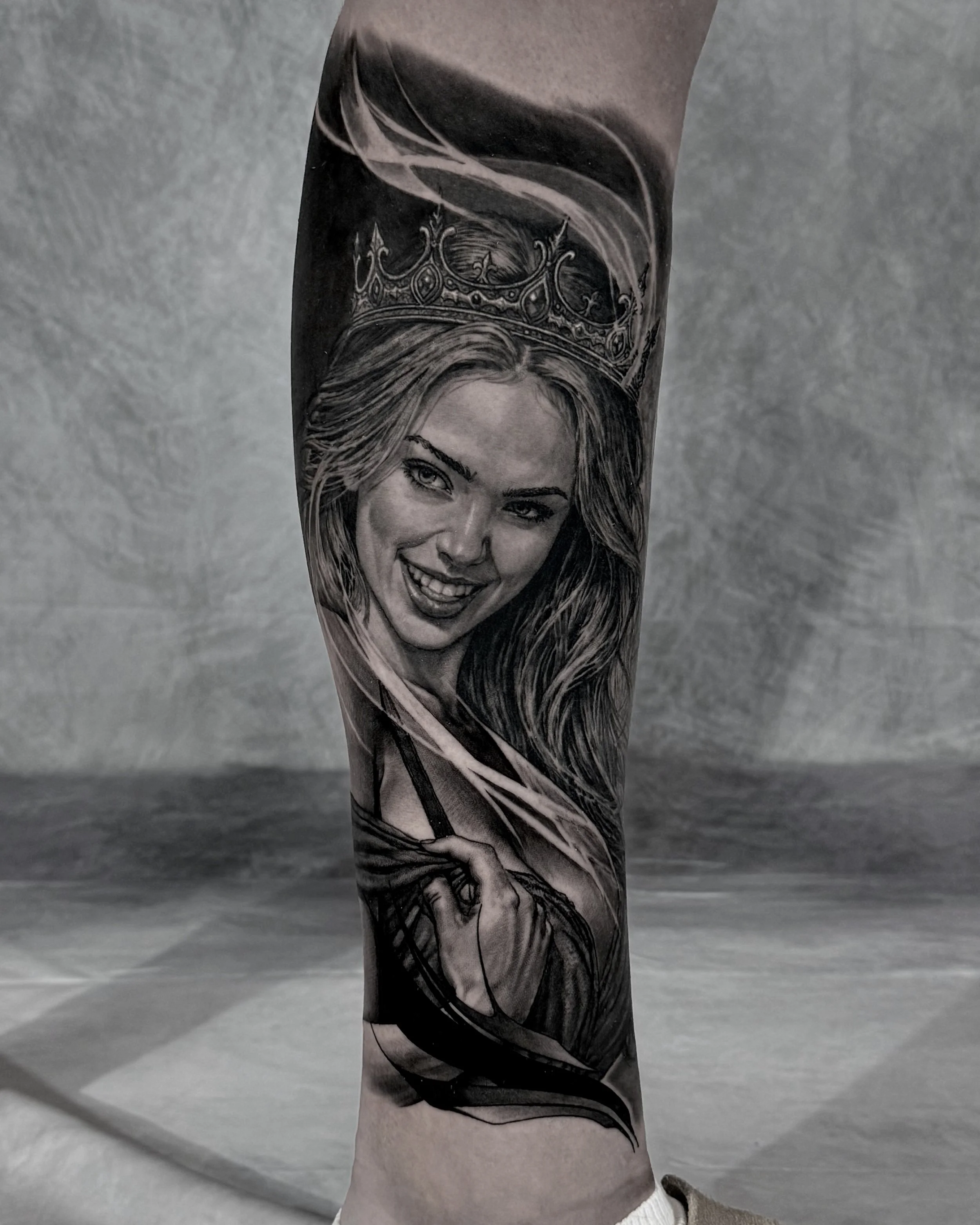 Smiling woman with crown portrait realism tattoo on the lower leg by Etgar Oak