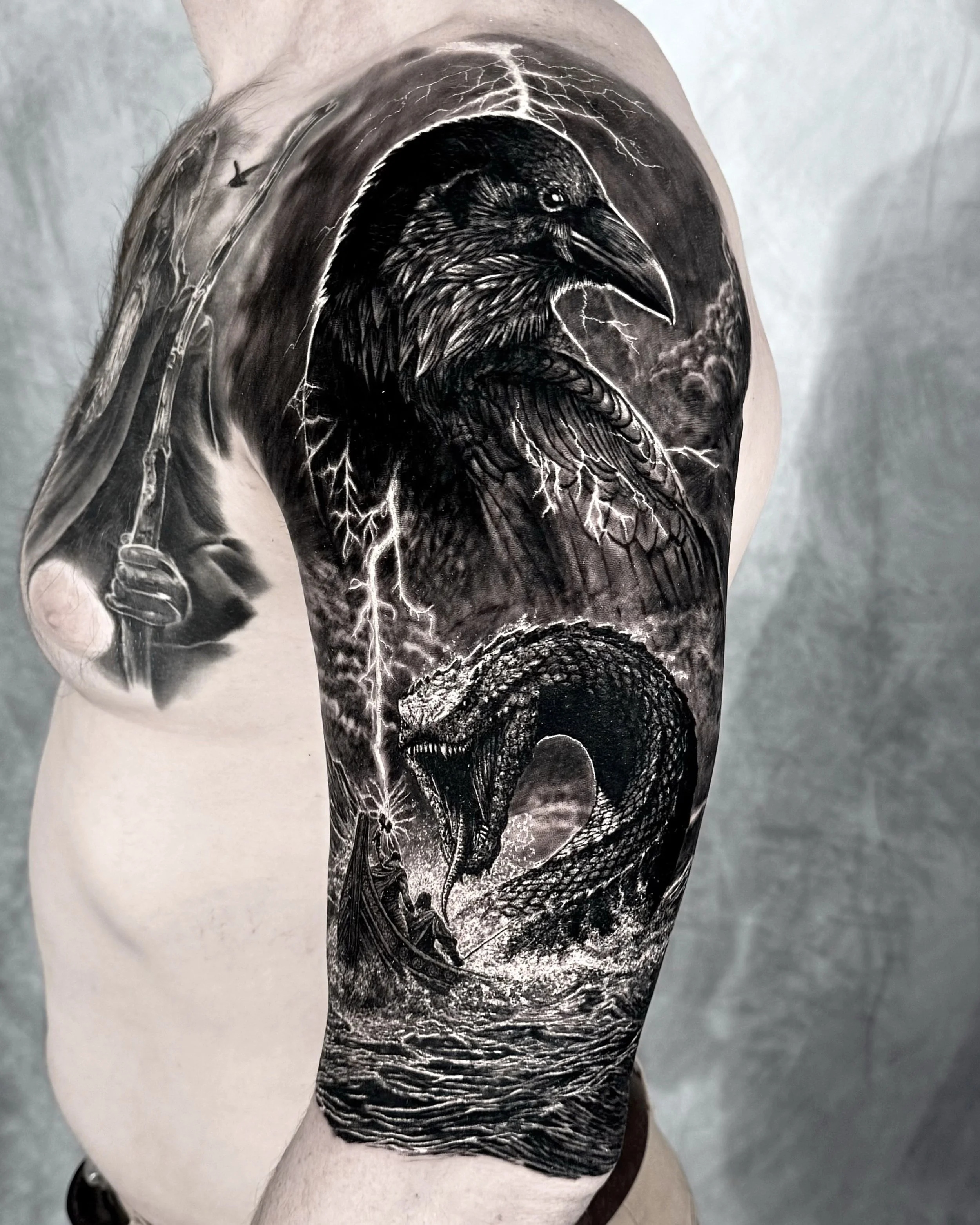 Raven, snake and lightning realism tattoo on the upper arm by Etgar Oak