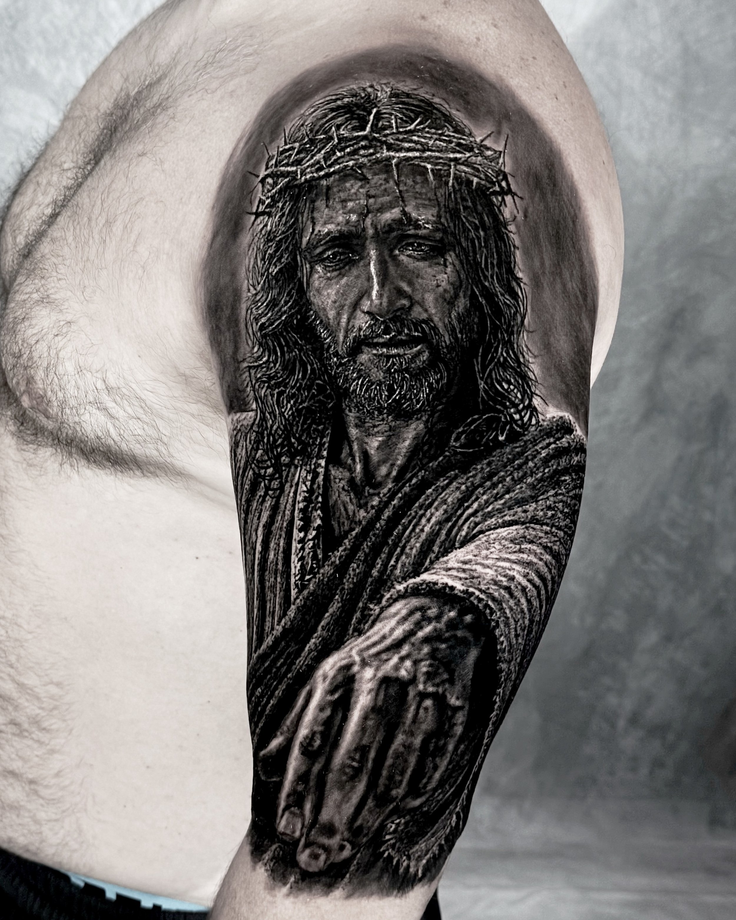 Jesus with crown of thorns reaching out his hand, realism tattoo on the upper arm by Etgar Oak