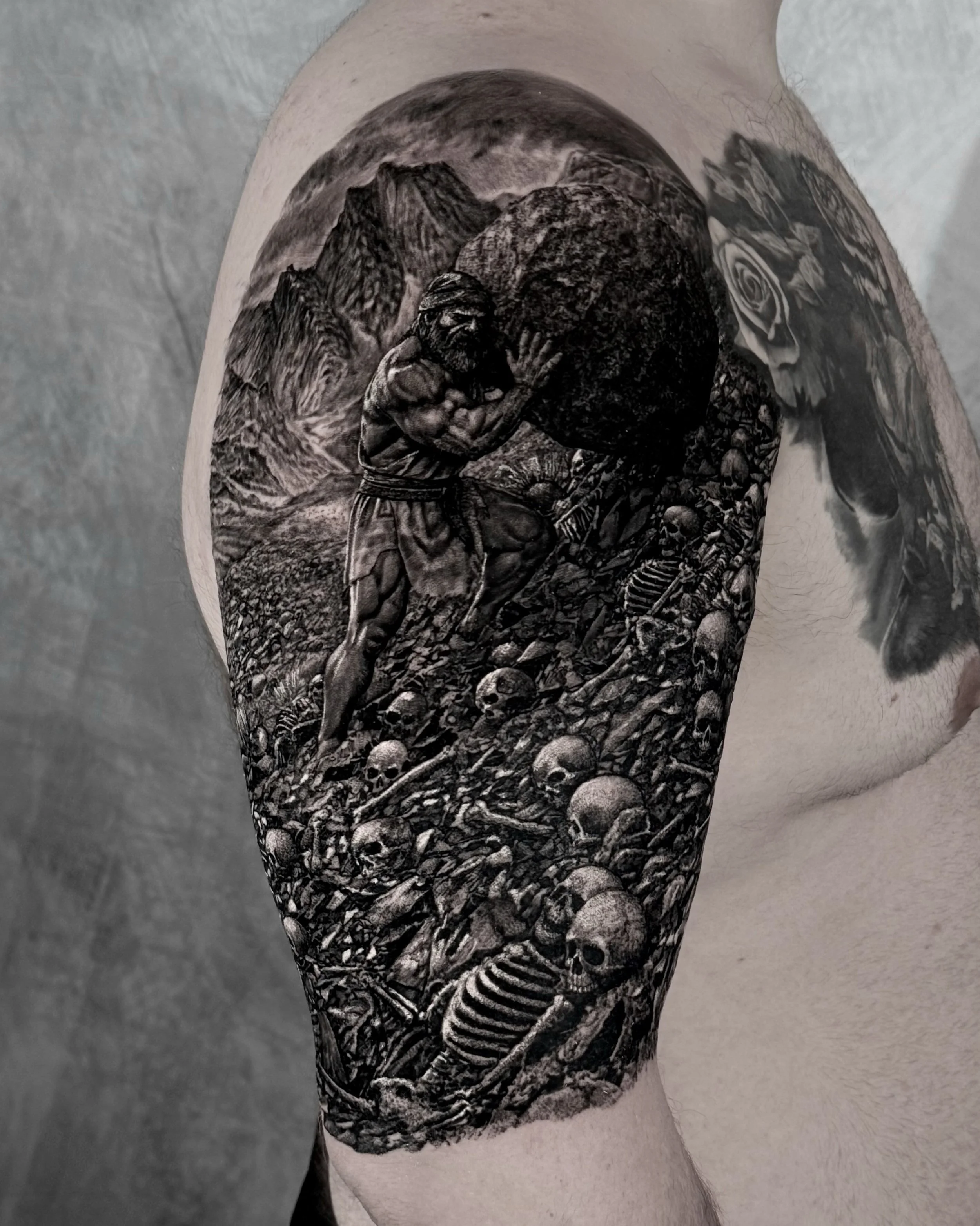 Sisyphus pushing a boulder over skulls realism tattoo on the upper arm by Etgar Oak