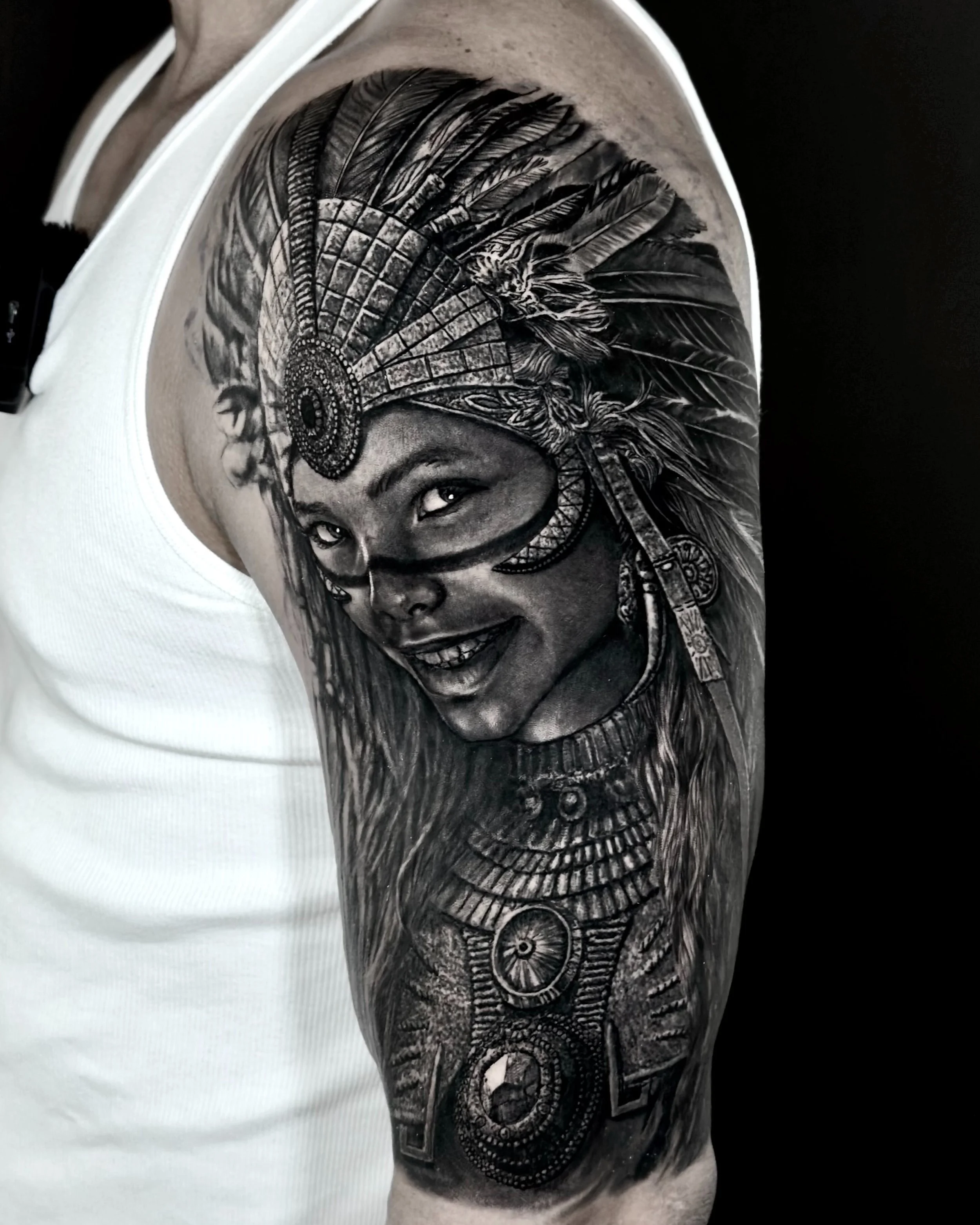 Woman in feather headdress realism tattoo on the upper arm by Etgar Oak