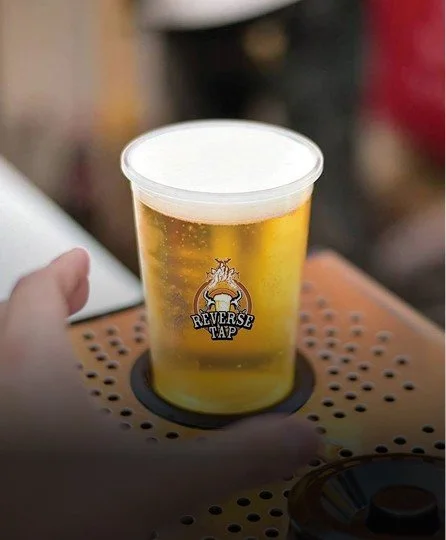 Clear plastic cup filled with light golden beer with a foamy white head, on a ReverseTap dispenser.