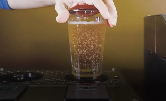 A hand holding a glass of beer on a bar counter.