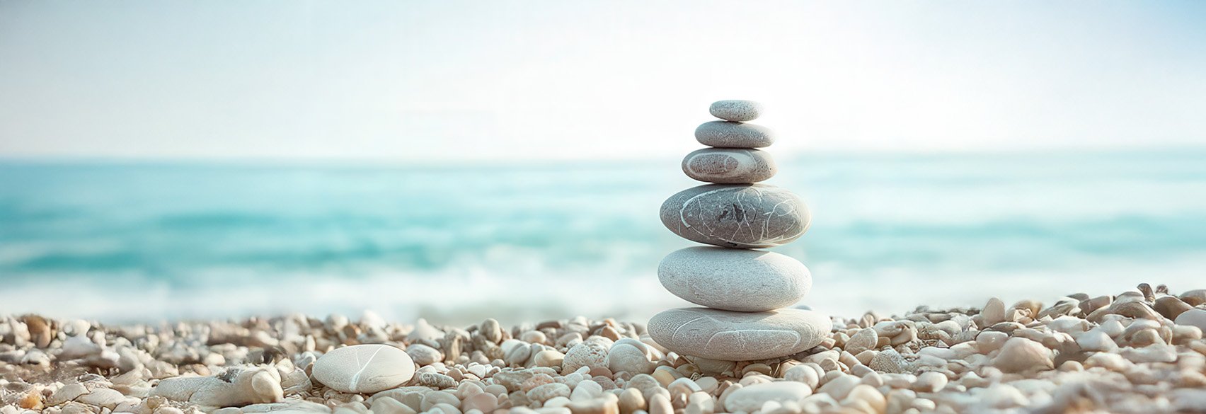 Stacked smooth gray stones on a bed of pebbles at the beach with the ocean in the background.