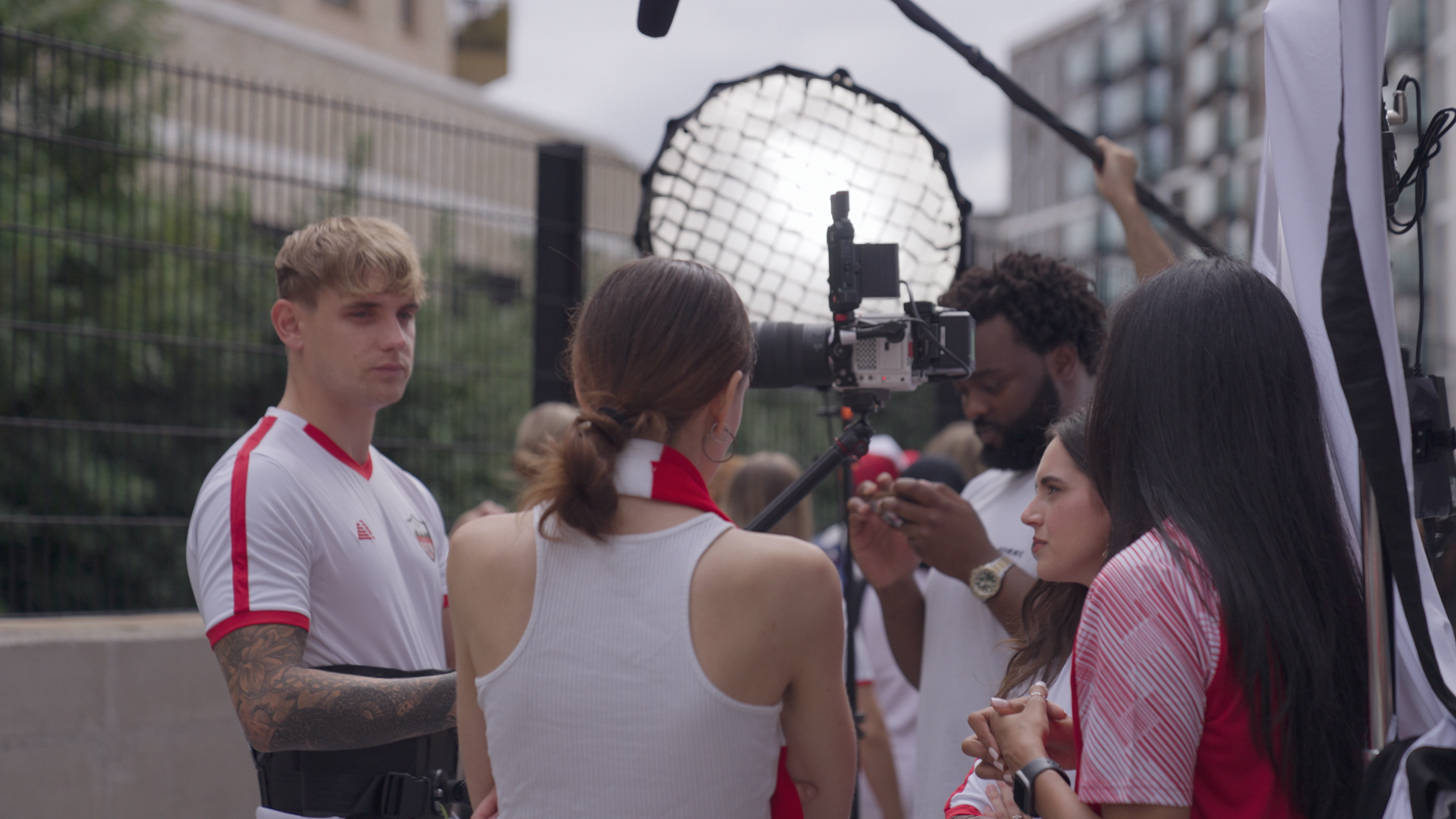 A sports interview or filming event outside with athletes and crew members, a camera operator, and professional lighting equipment.