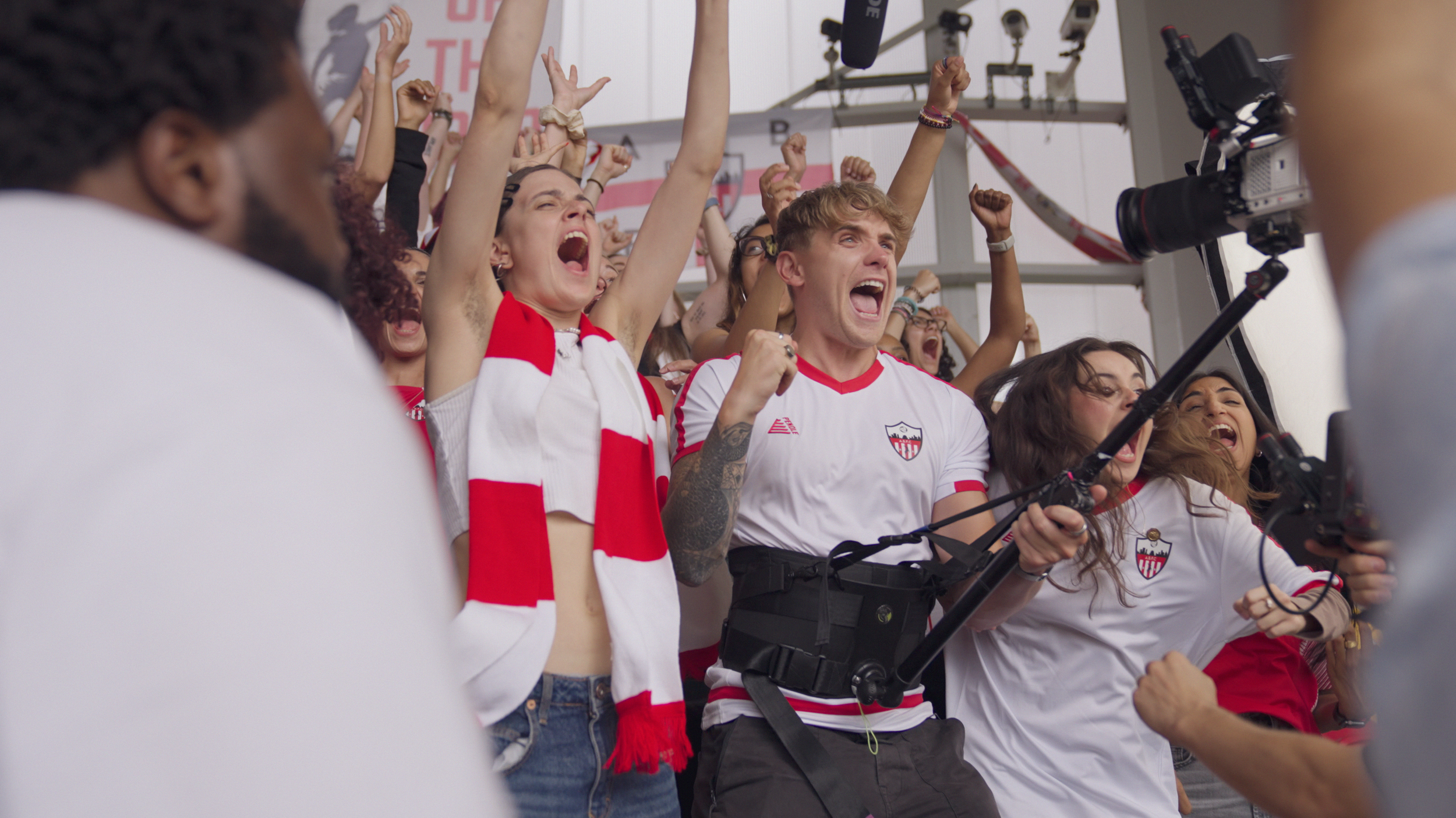Group of excited sports fans celebrating, wearing team jerseys, holding cameras, and cheering with raised fists.
