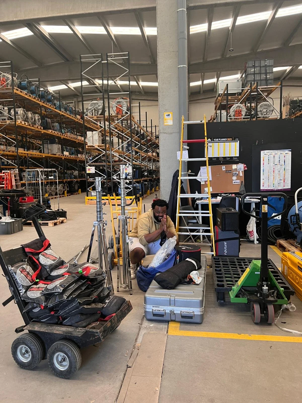Man crouching next to equipment and tools in a warehouse or hardware store, with shelves filled with various machinery and items in the background.