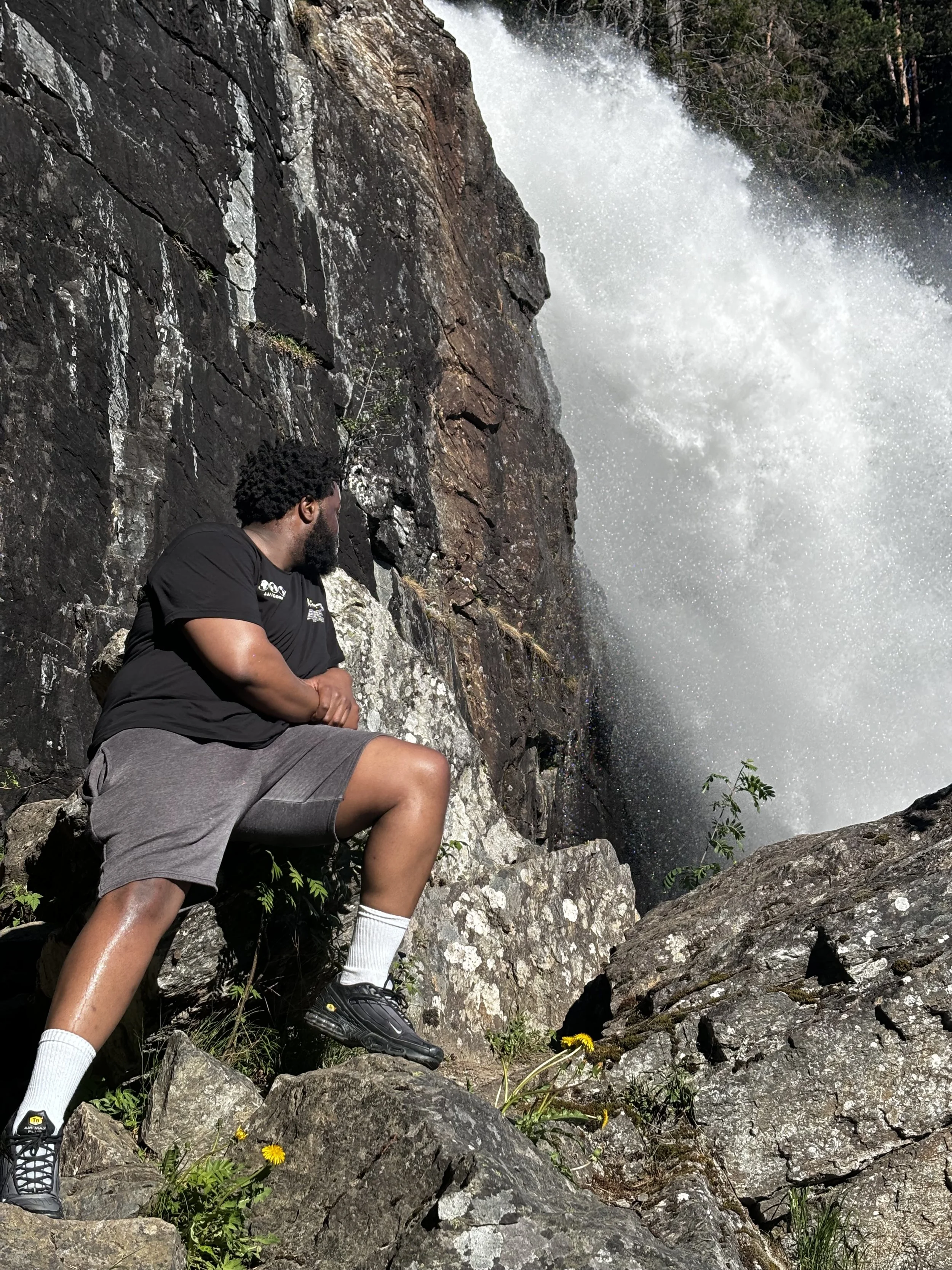 A man sitting on rocks near a waterfall, looking at the cascading water.