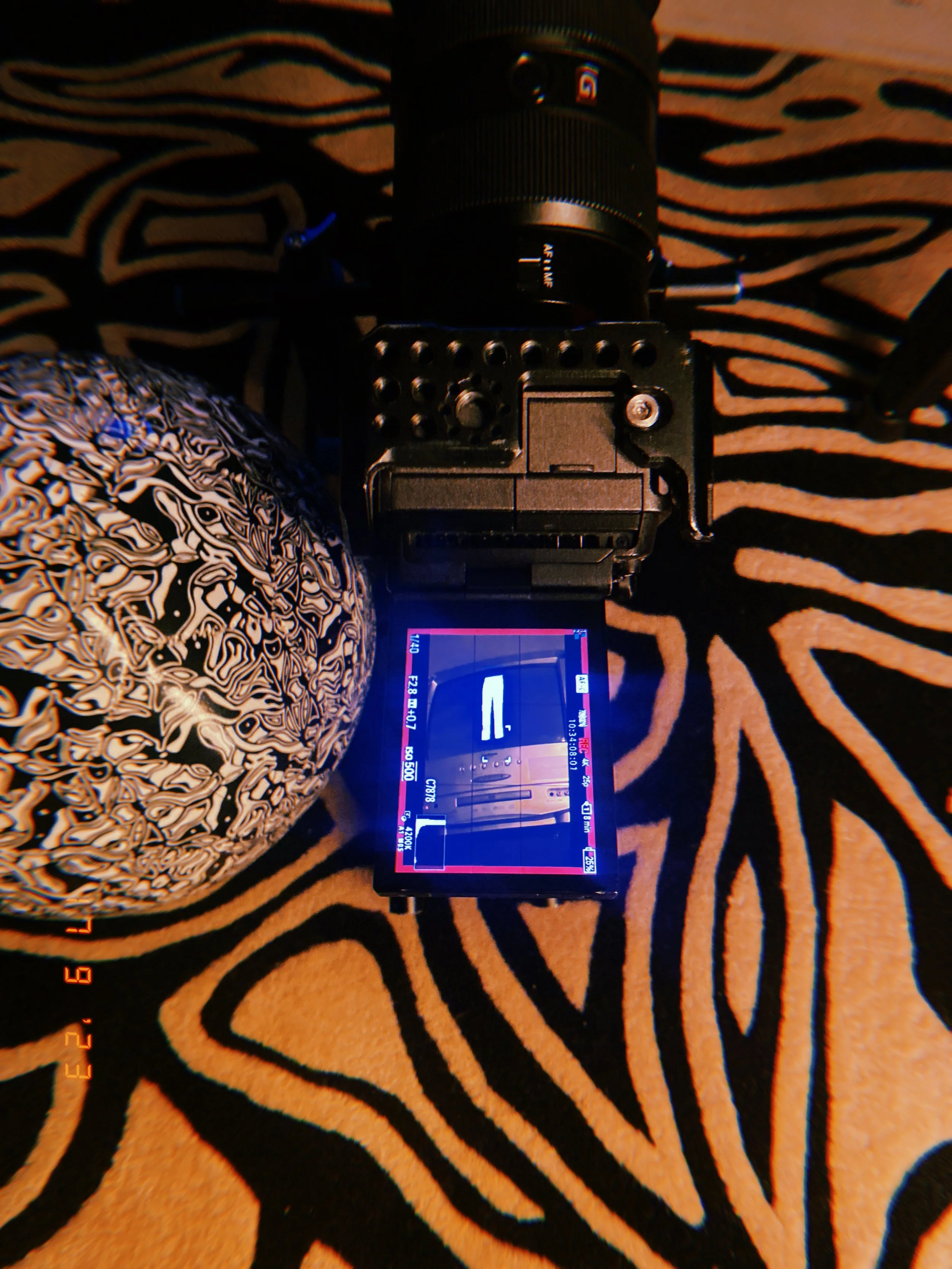 Camera with digital screen, black patterned object, and zebra print surface with black and beige stripes.