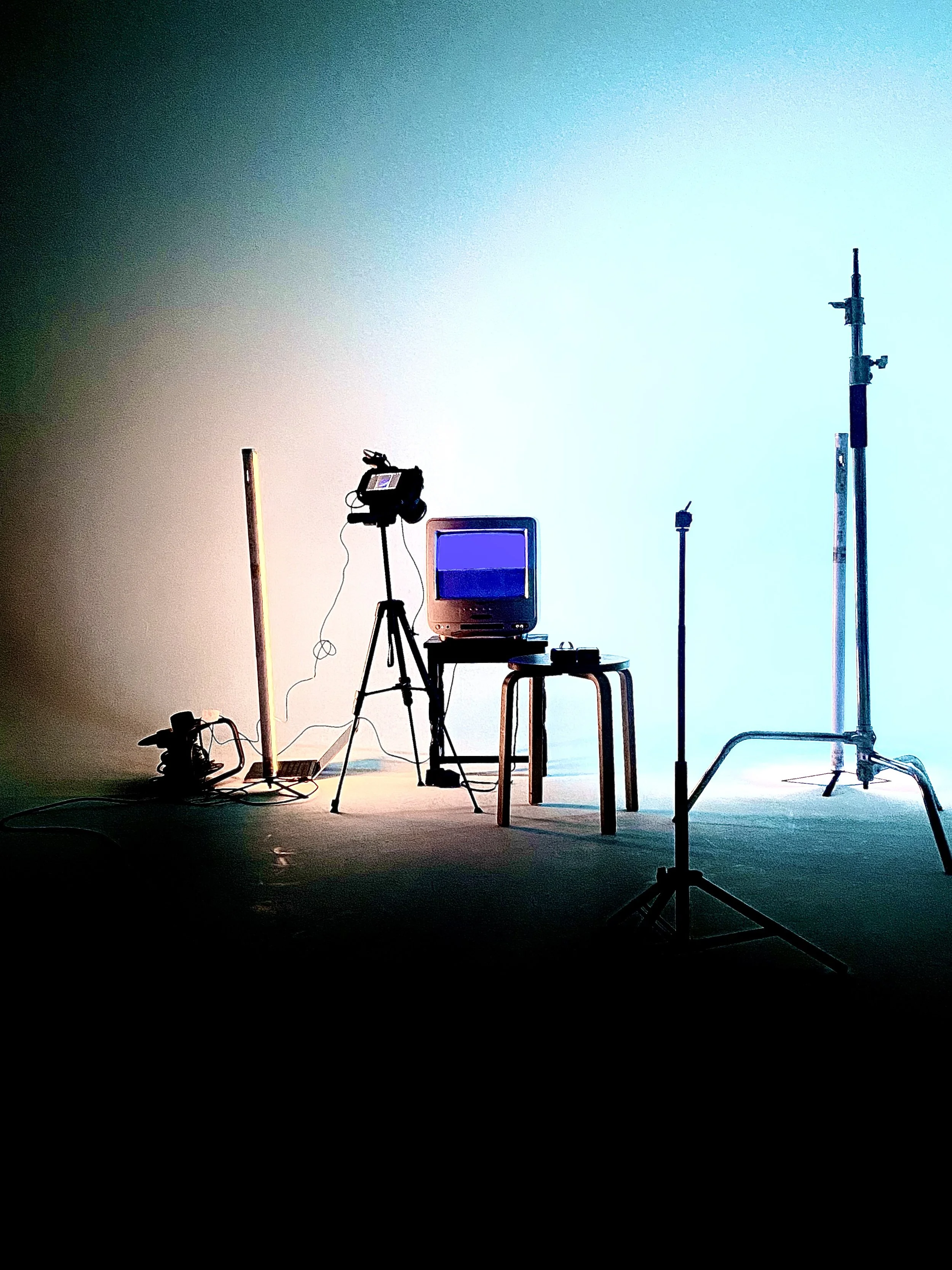 Empty photography studio setup with lighting and camera equipment, television, stool, and background stand, lit by colorful lights.