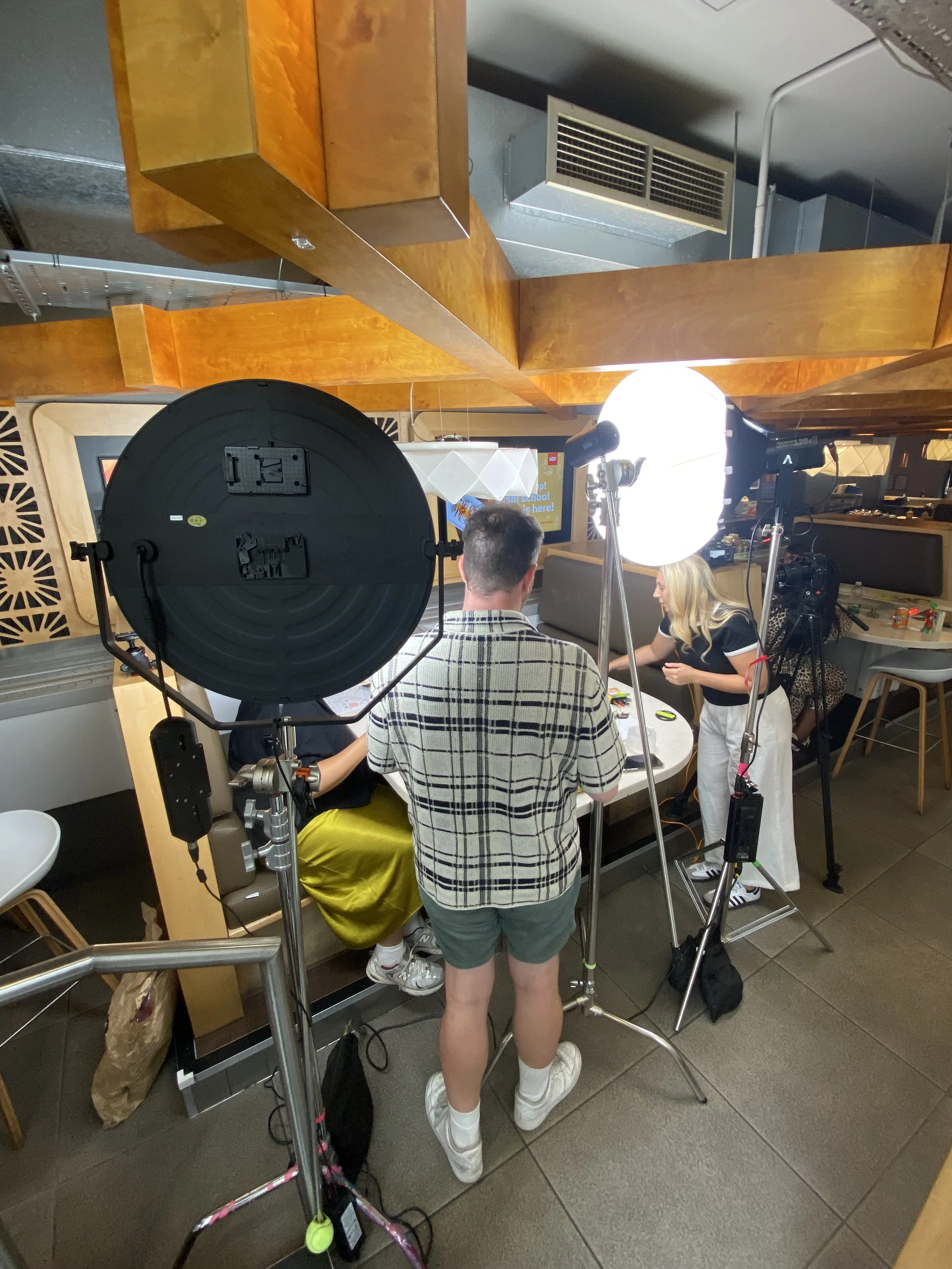 Filming a group of people at a table in a restaurant with professional lighting and camera equipment.