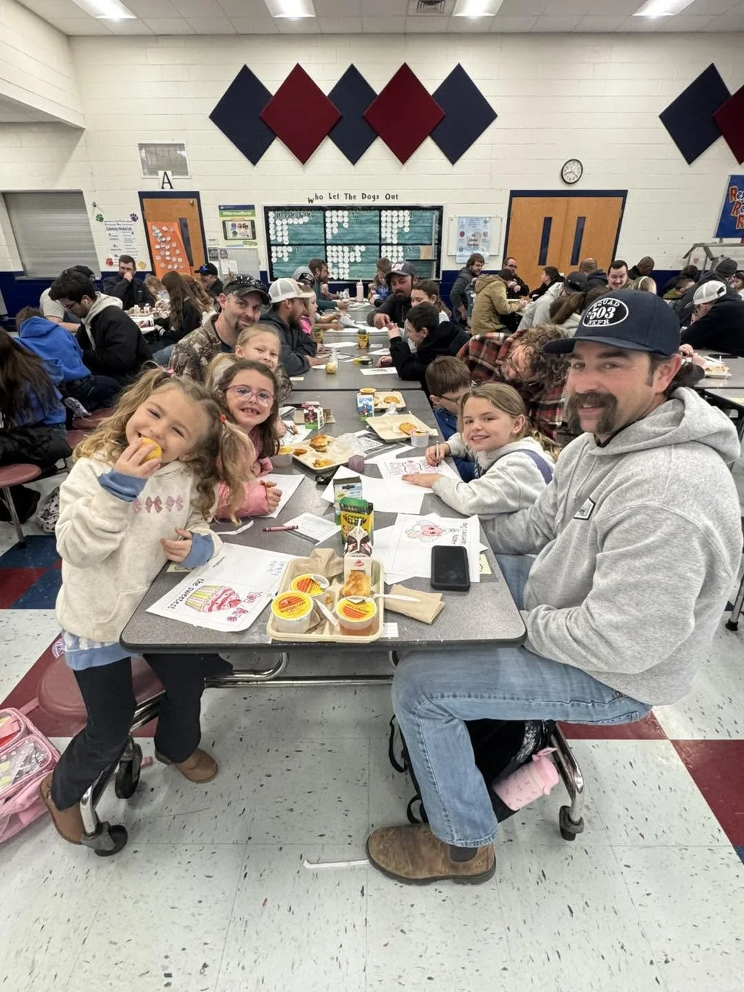 Children and families sitting at a table in a cafeteria