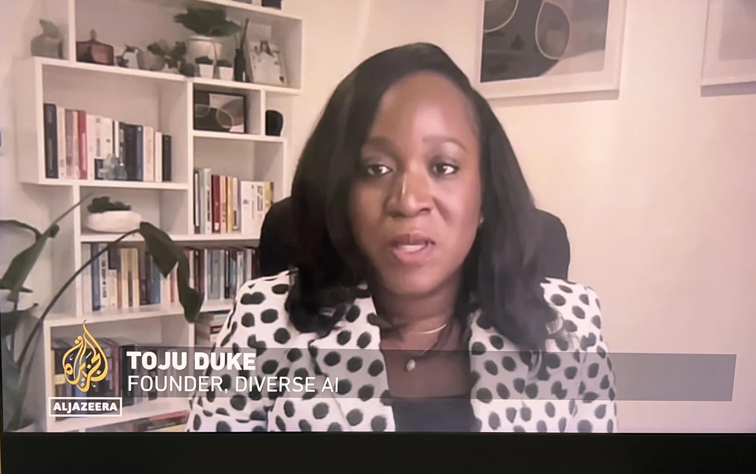 Toju Duke, founder of Diverse AI, speaking in an interview with Al Jazeera in a room with bookshelves and plants in the background.