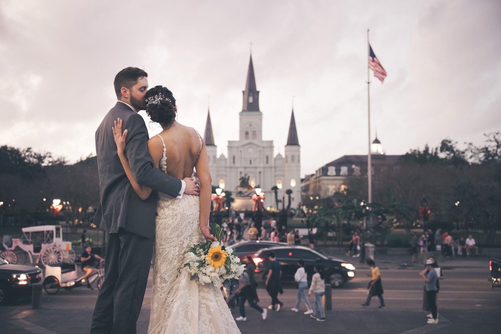 Bride and groom in front of St. Louis Cathedral, New Orleans, with people and cars in the background.