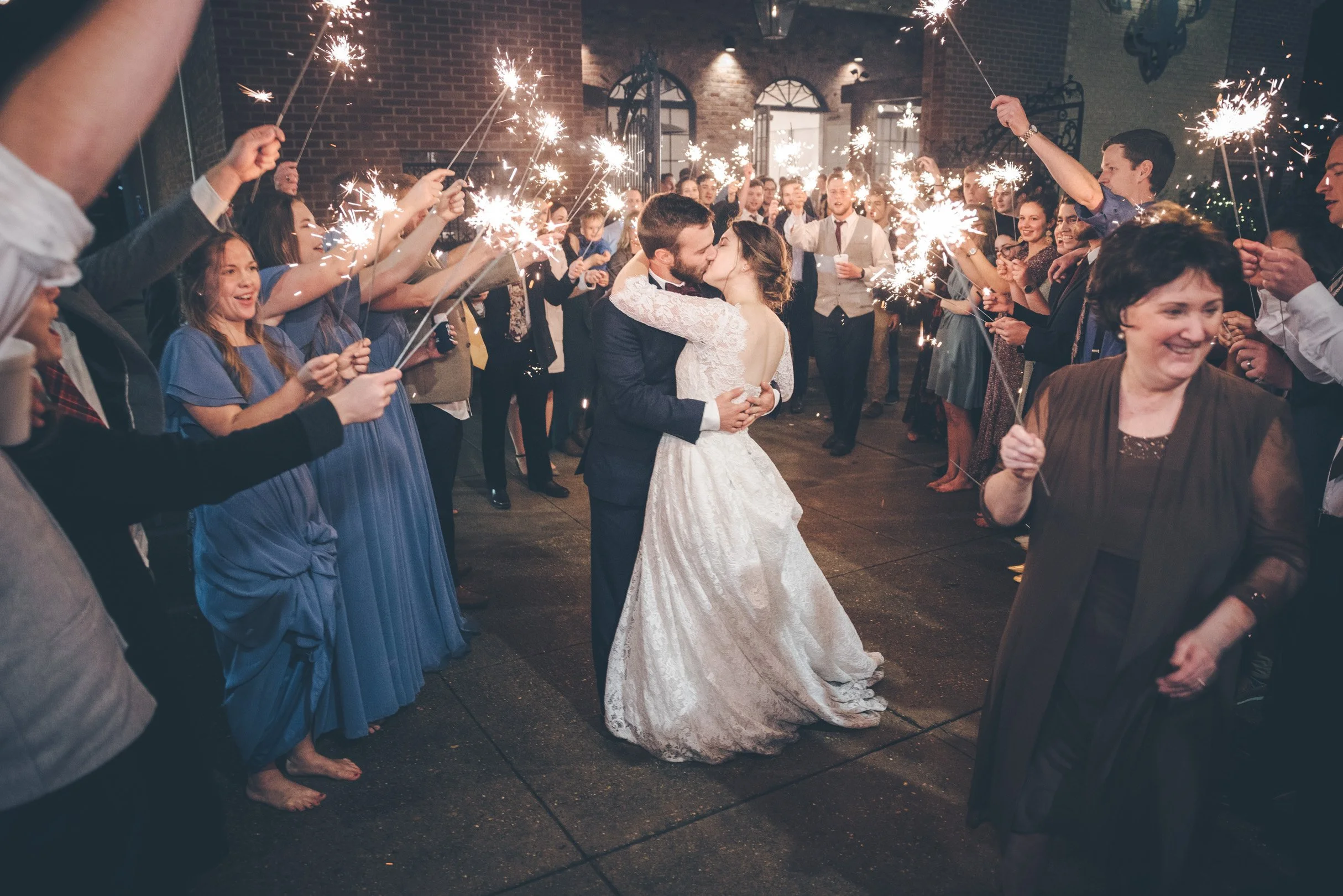 Bride and groom kissing surrounded by guests holding sparklers at a wedding reception.