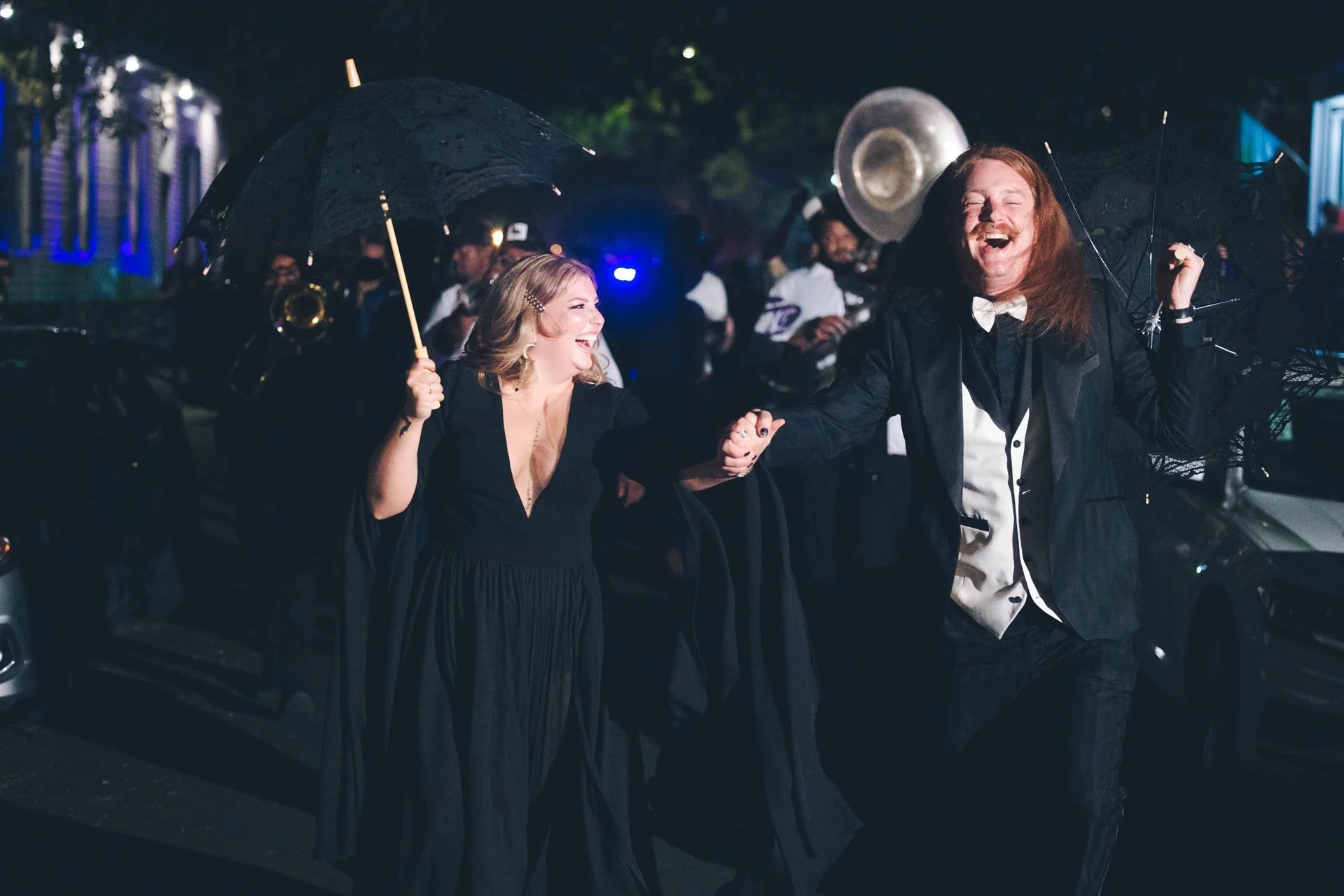 Couple celebrating with a brass band parade at night, holding umbrellas.