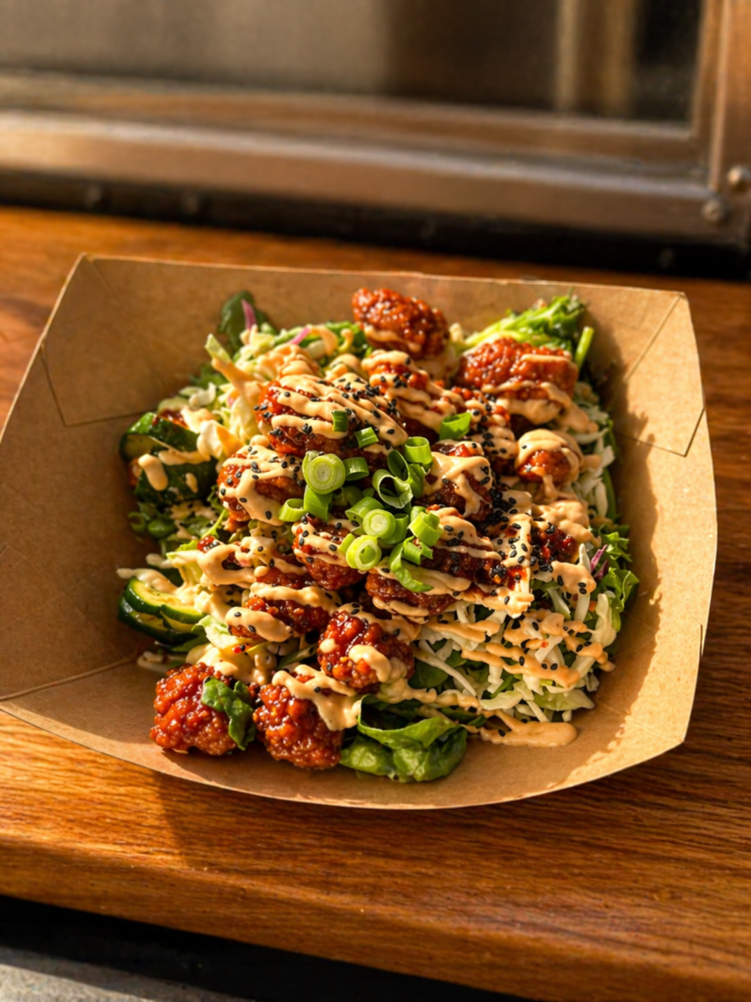 Korean fried chicken bowl with slaw, cucumber and chili aioli drizzle in warm window light