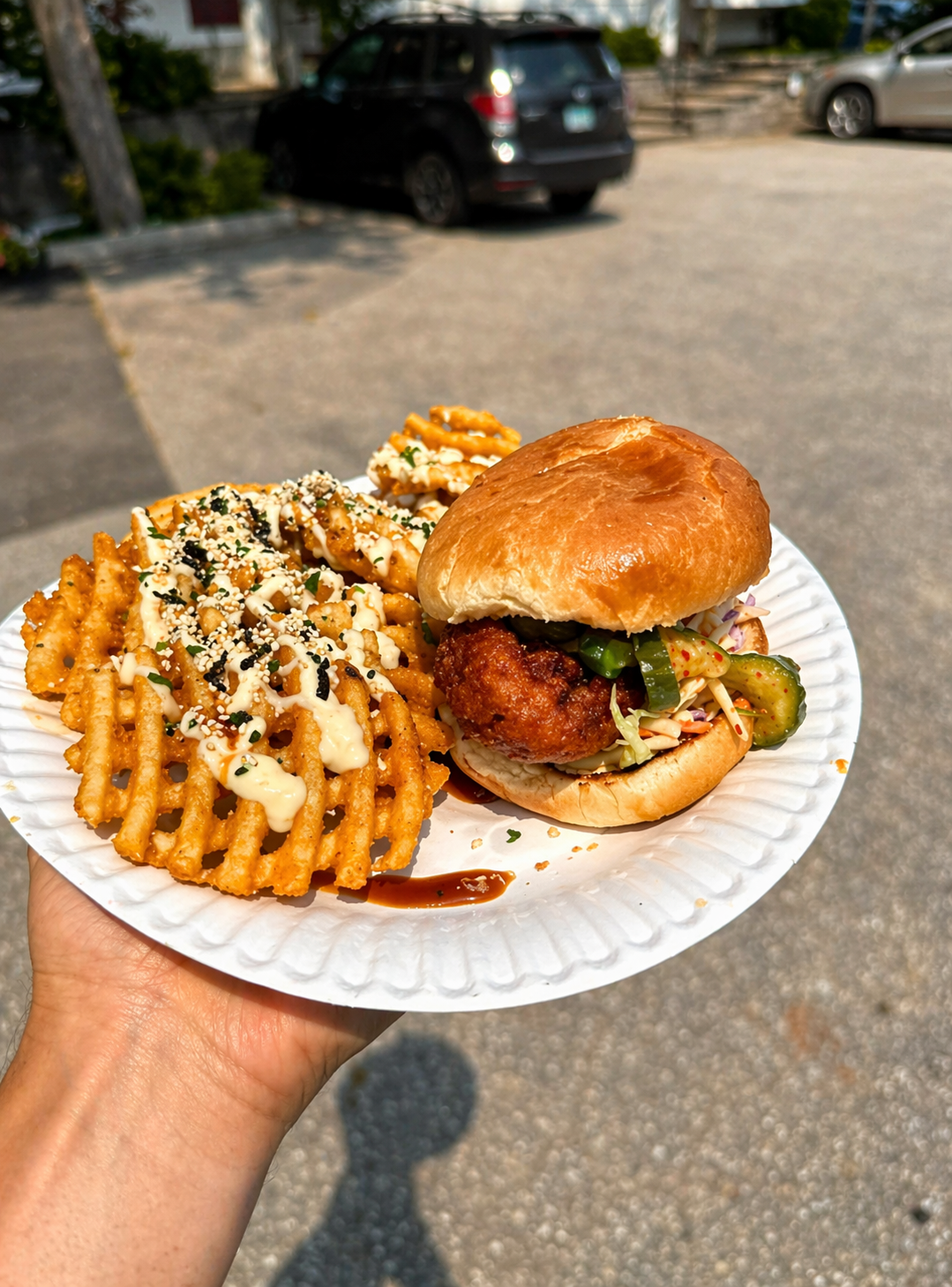 Fried chicken sandwich on a brioche bun with Tokyo street fries on a paper plate in the sun