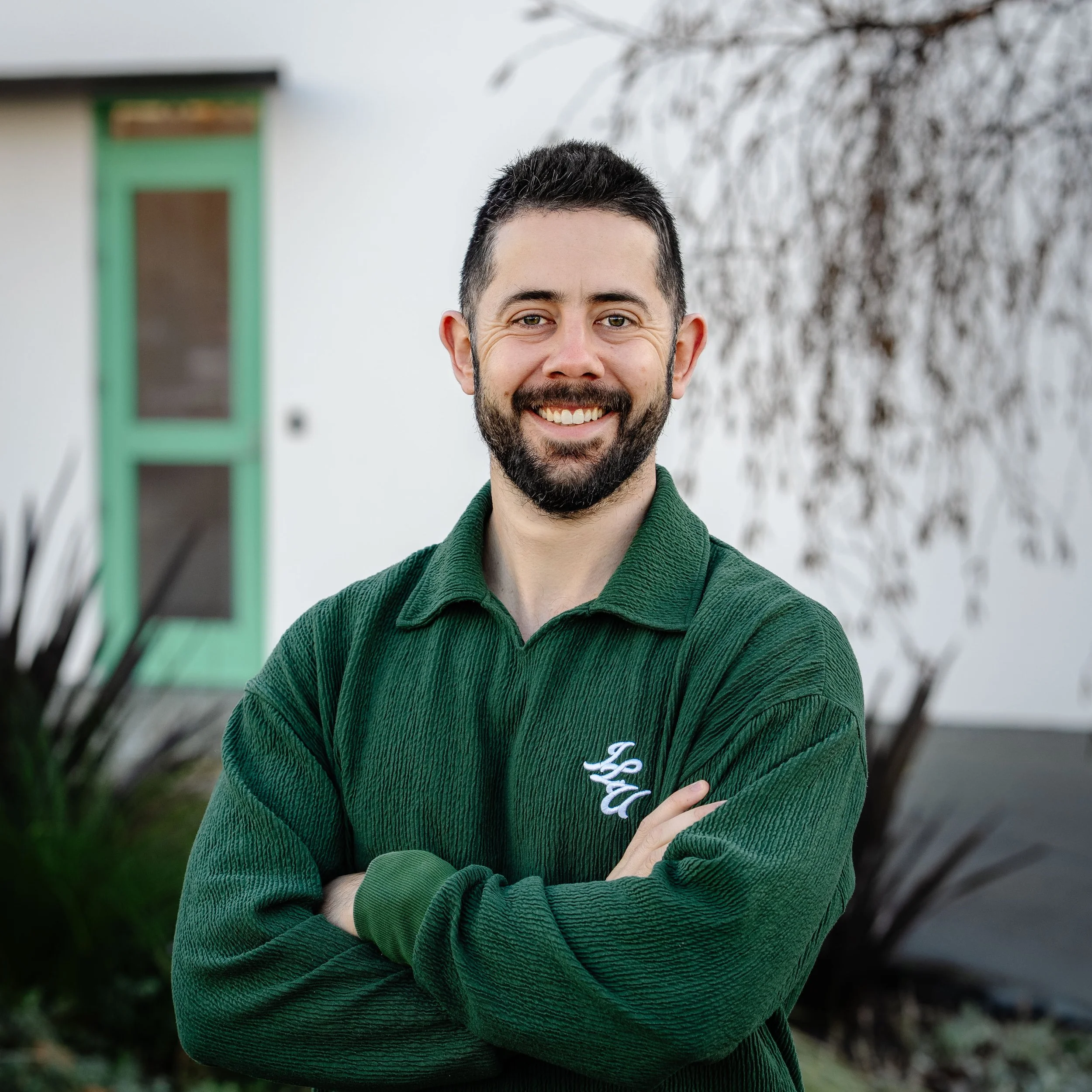 Head shot of Kurt Hay smiling wearing white tee and black shirt jacket with trees in background.  