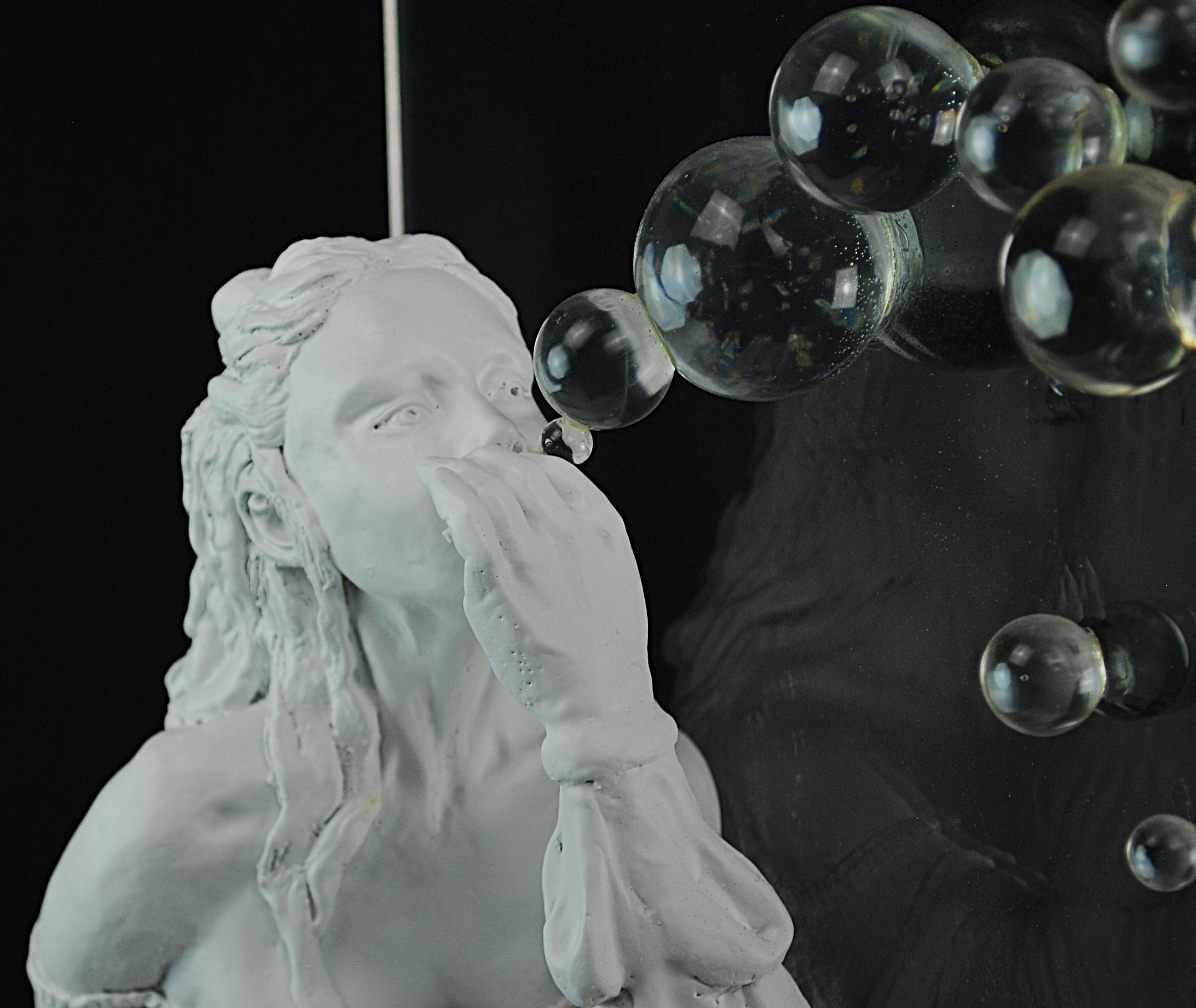 Souffleur une Bulles sculpture by Sharon Cruson, seated woman blowing bubbles against a dark background