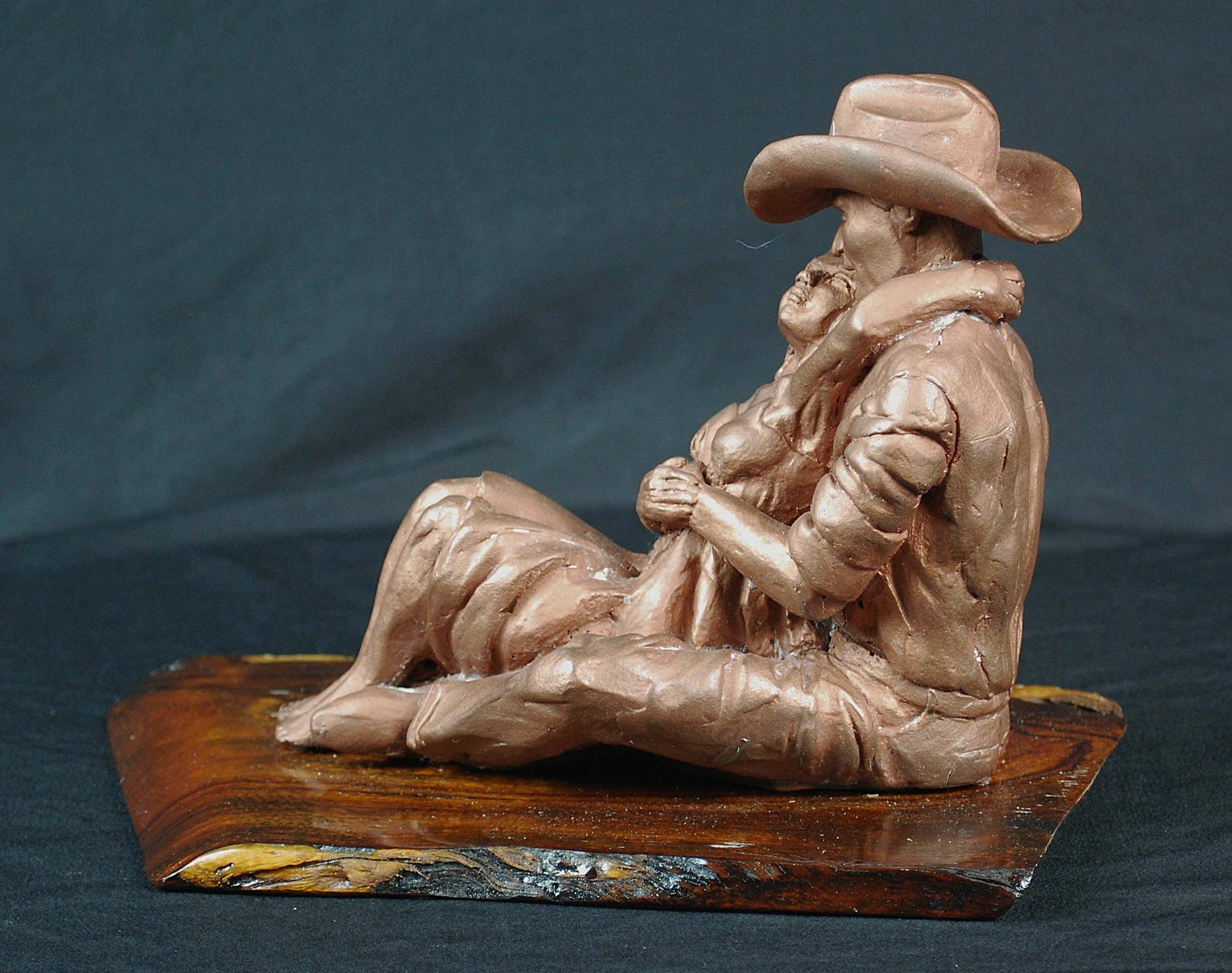 Cowboy Couple sculpture by Sharon Cruson, side view of seated Western couple on natural wood base