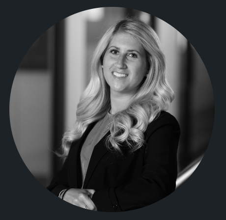 Black and white professional portrait of a woman with long wavy blonde hair, wearing a blazer and smiling.