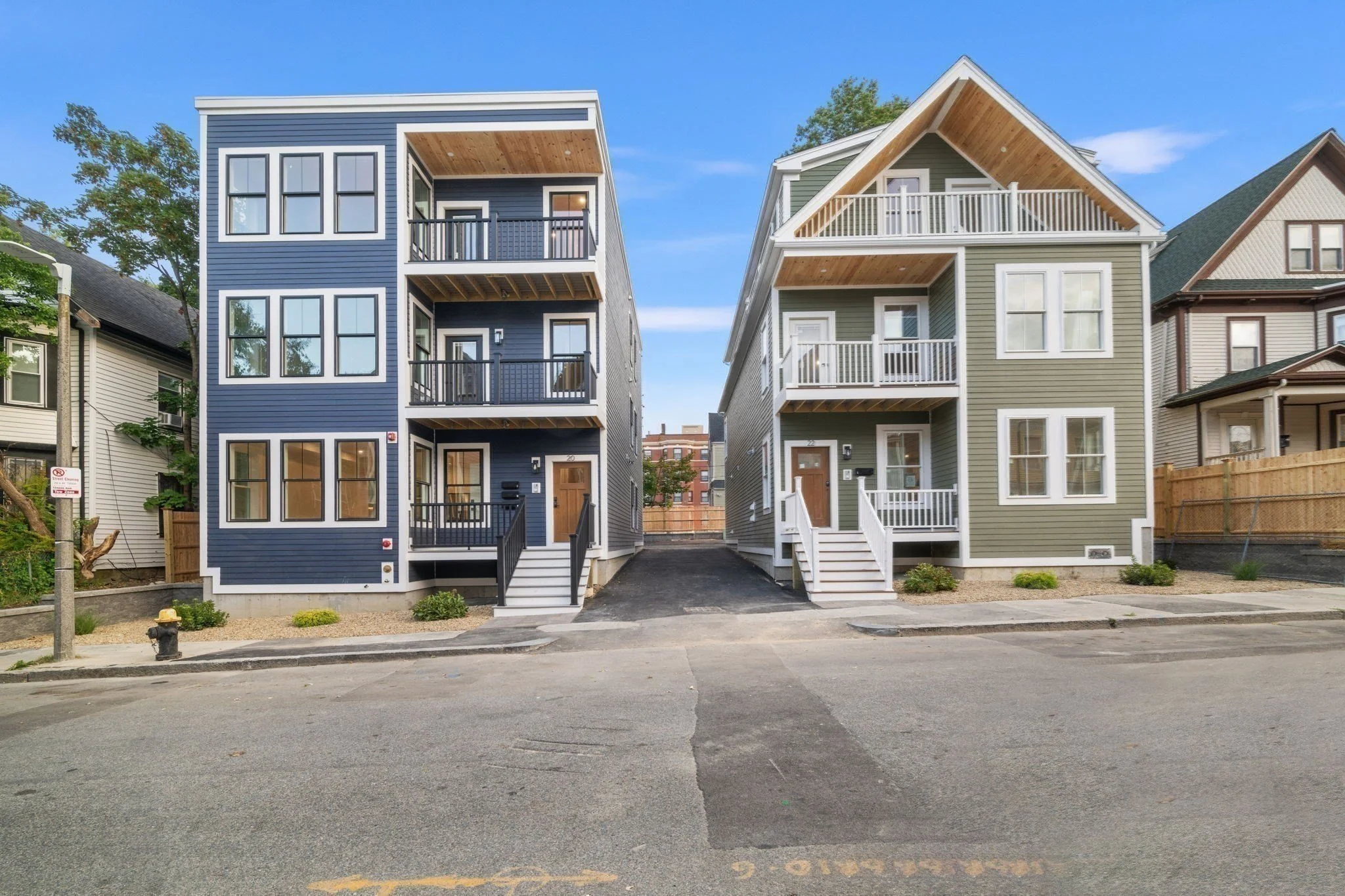 Two modern multi-story residential buildings facing the street, with front entrances and small balconies, separated by a narrow driveway.