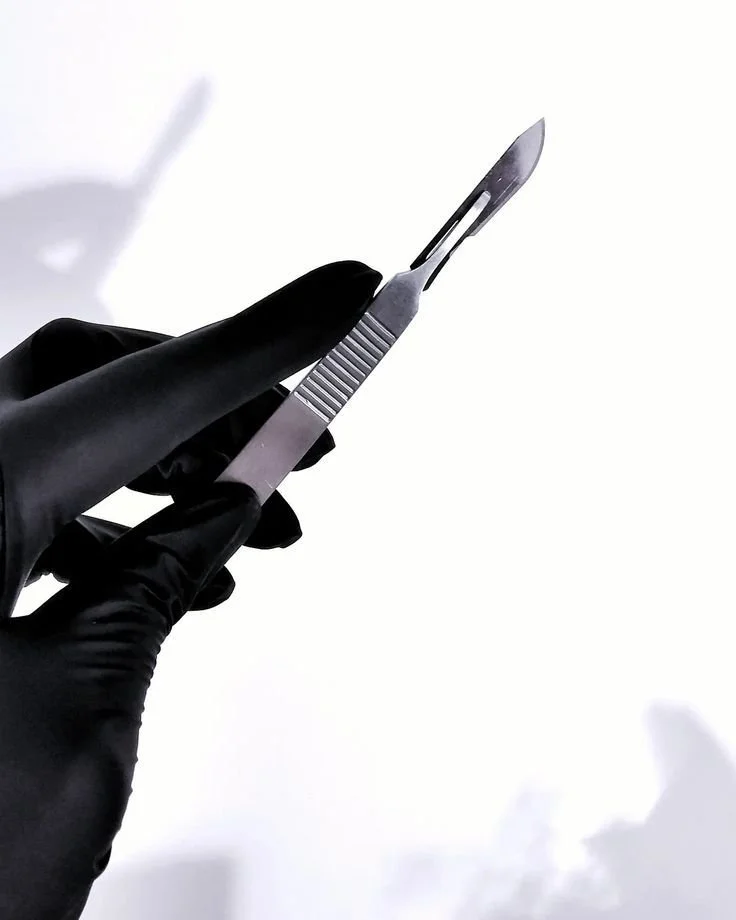 Hand in black glove holding a surgical scalpel against a white background.