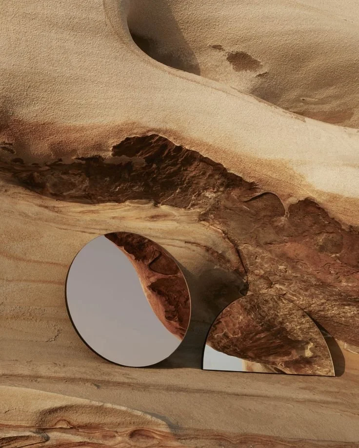 Circular and semi-circular mirrors placed on a textured beige and brown stone surface reflecting part of the rock formation.