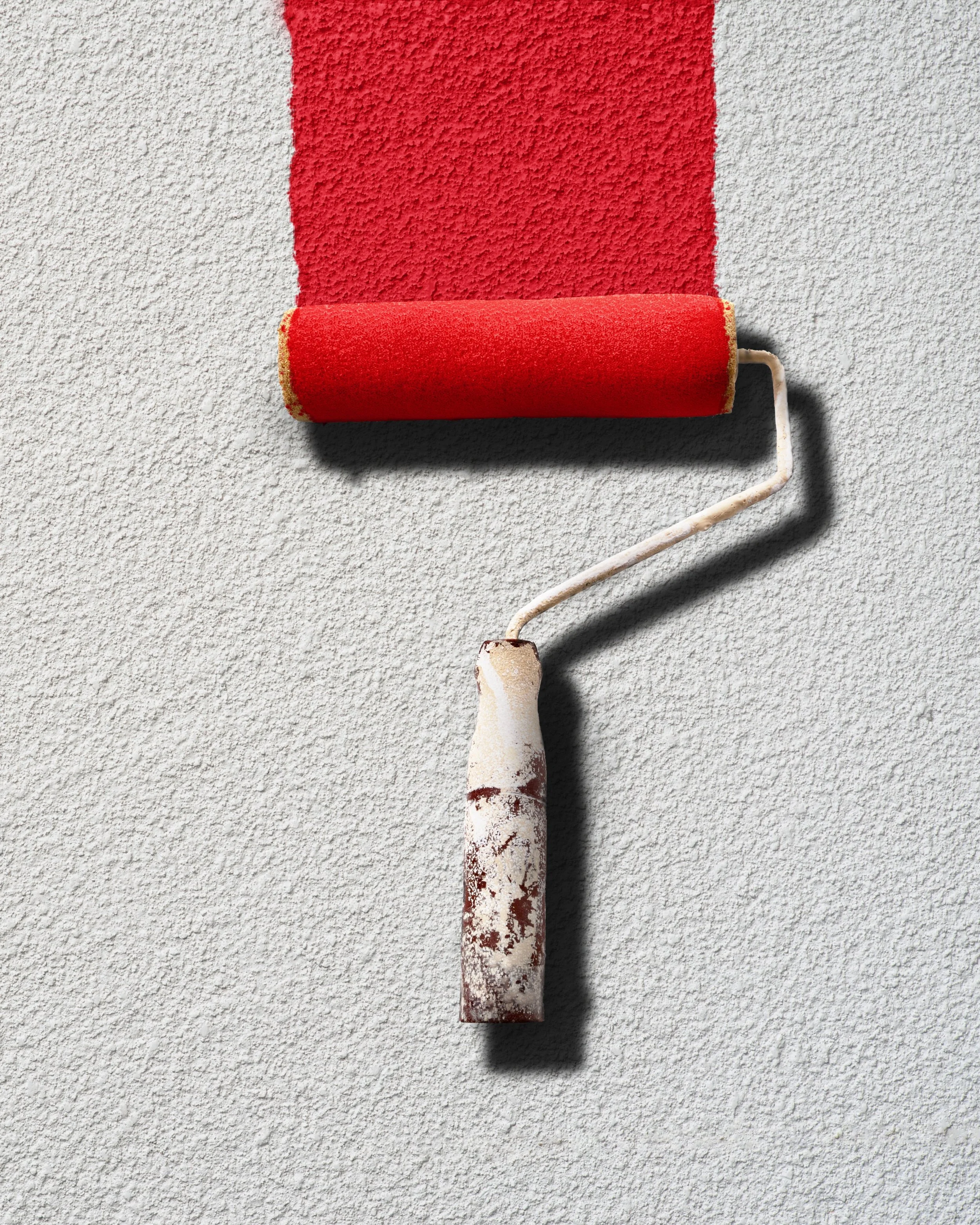 A paint roller with a red roller cover, partially painted on a textured light gray wall.