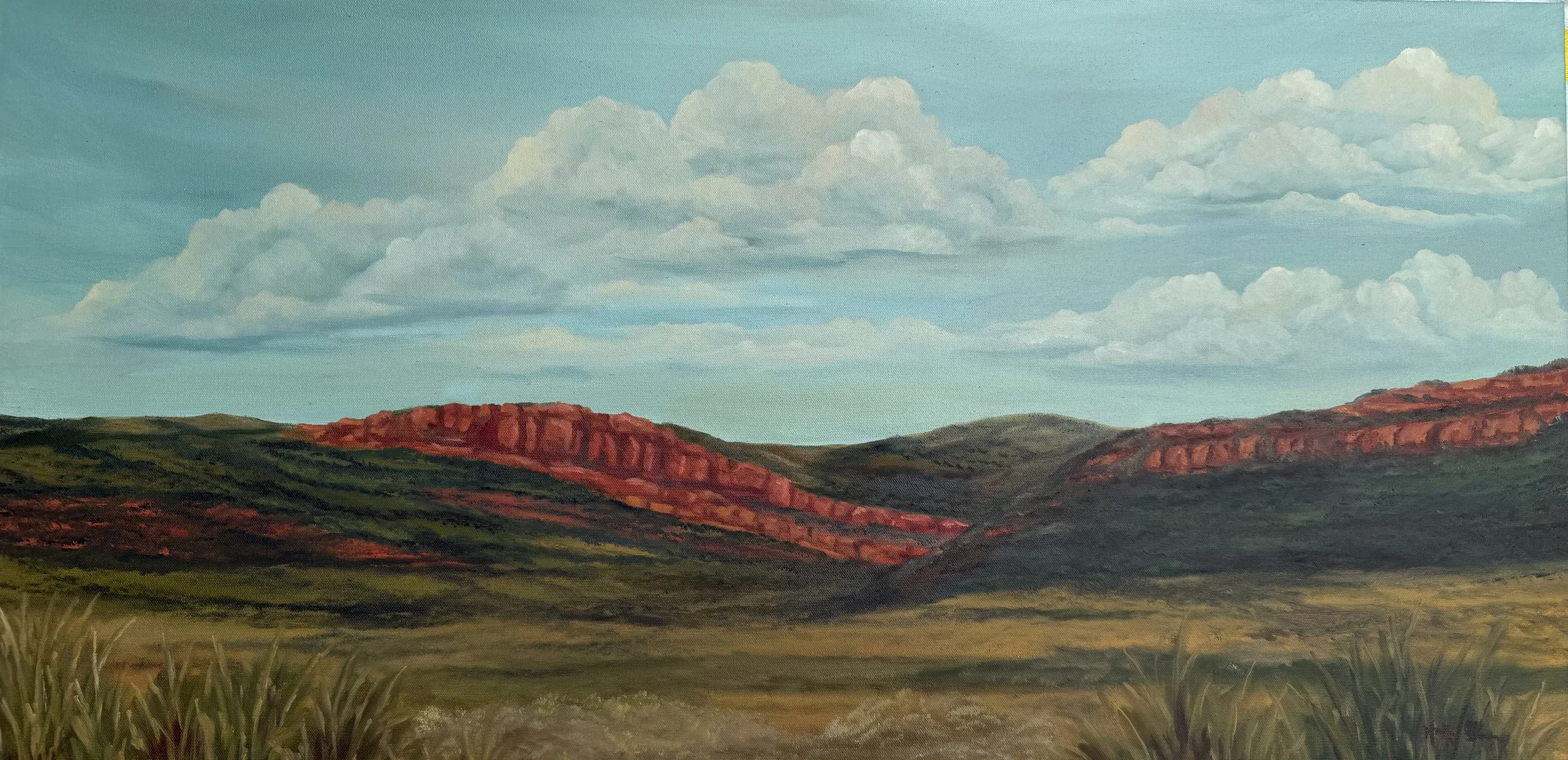 A painting of a landscape with red rock formations in the distance, green hills and grass in the foreground, and a blue sky with scattered clouds.