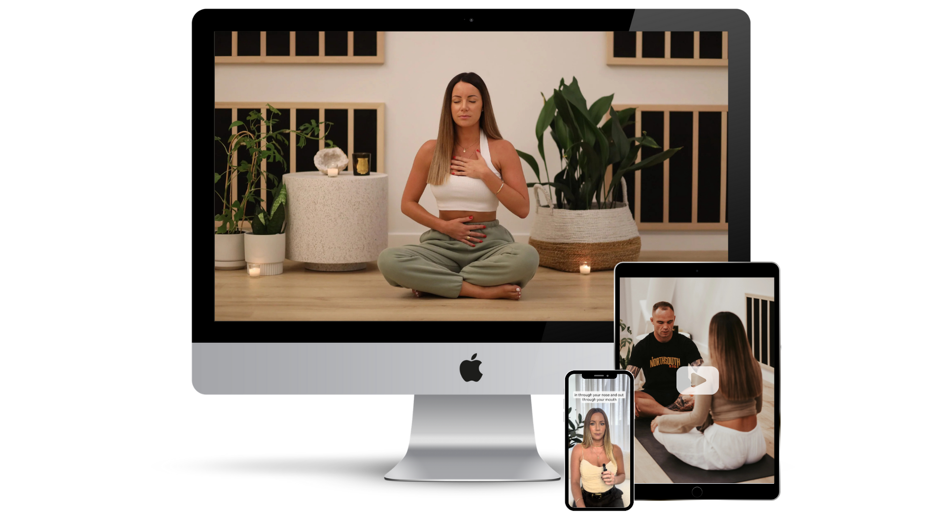 A woman sitting cross-legged on the floor meditating with her hand on her chest and stomach in a serene indoor space, surrounded by plants and candles, displayed on various digital devices.