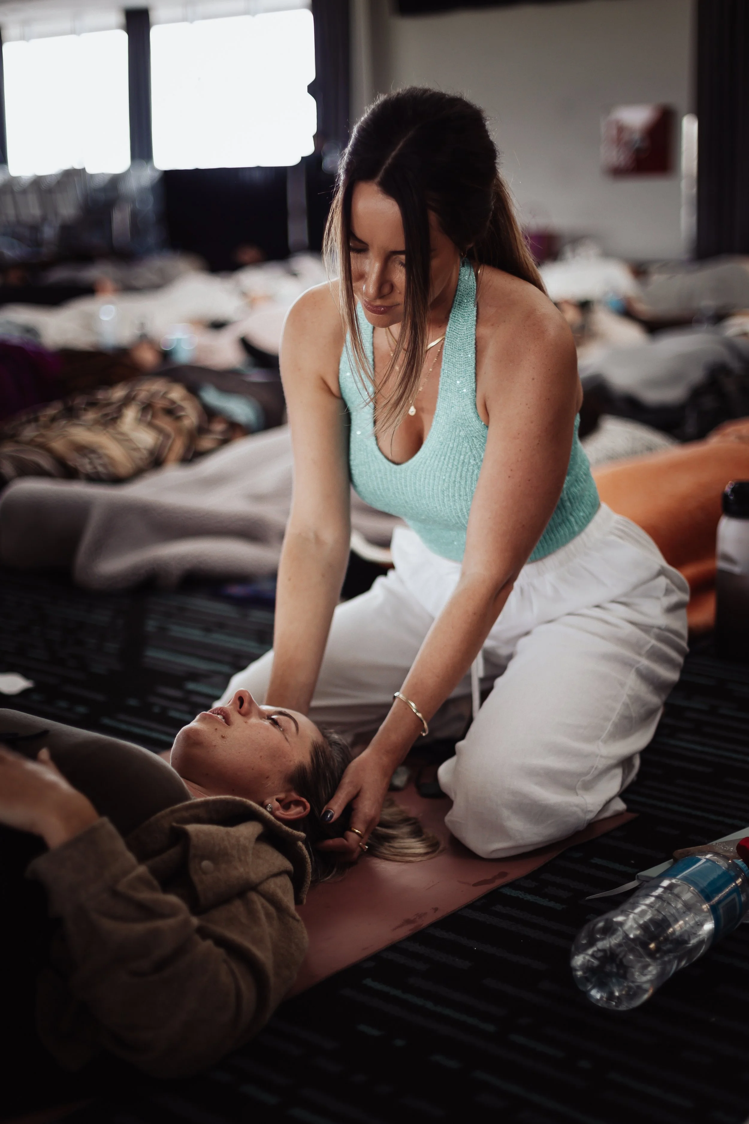 A woman performing CPR on another woman lying on the floor in a room with many beds, likely a medical or care facility.