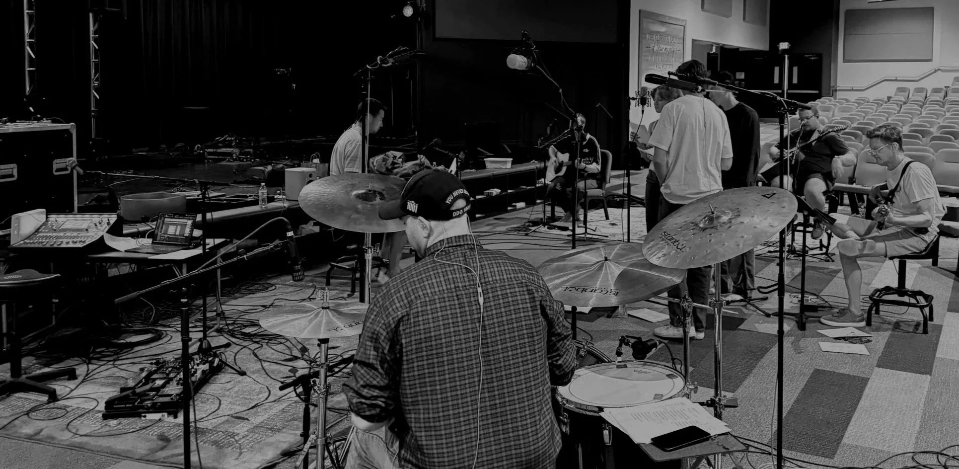 Musicians and sound crew preparing in a rehearsal space for a performance, with musical instruments, microphones, and audio equipment.