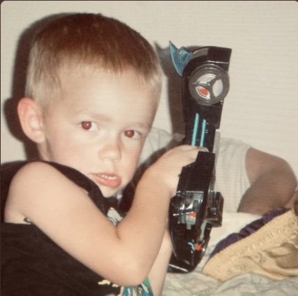 Young boy holding a large toy gun with a blue and gray design, indoor setting.