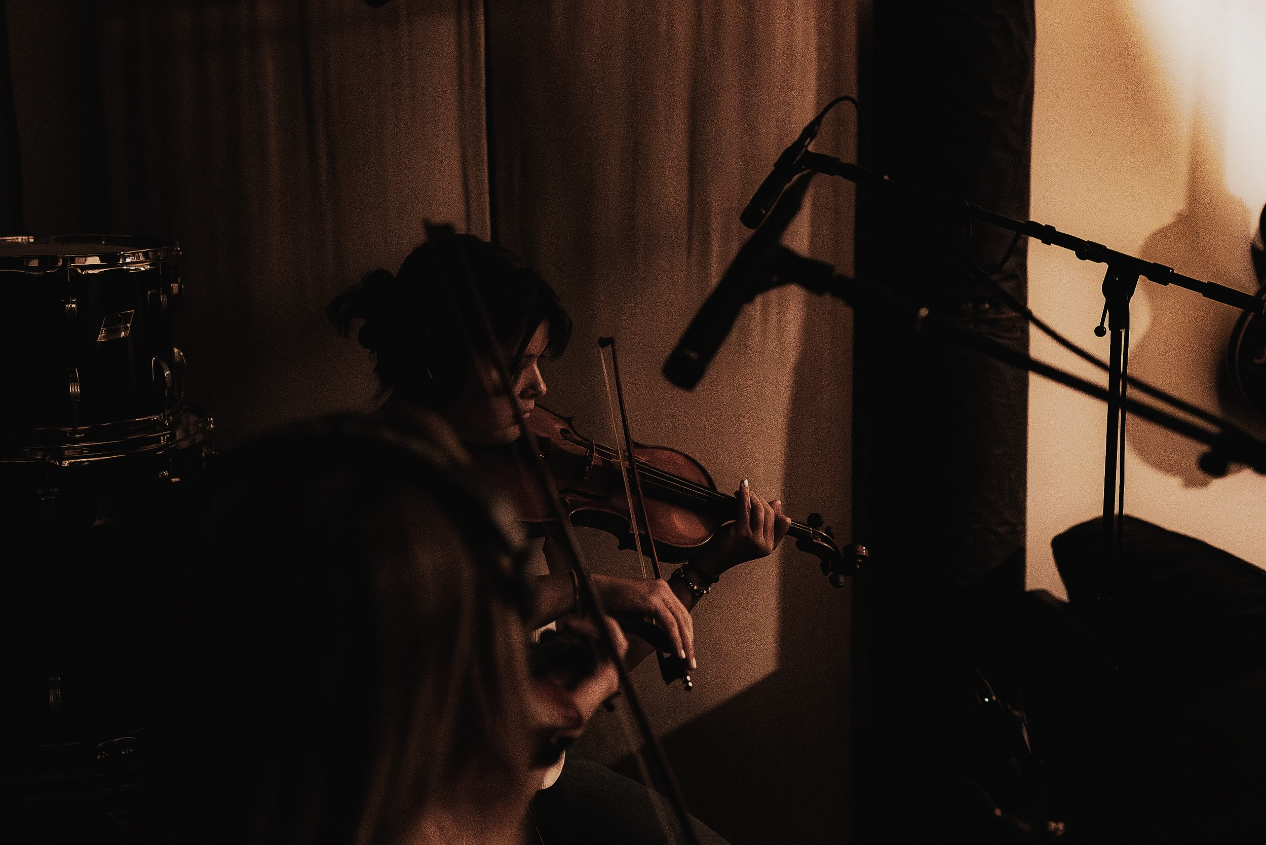 Female violinist performing during a live music recording session, surrounded by microphones and instruments in a warmly lit studio. Copy Alt Text