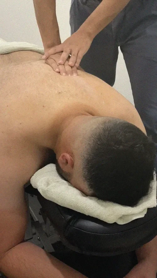 A remedial massage therapist in Liverpool applies pressure to the mid back of a man lying face down on a treatment table.
