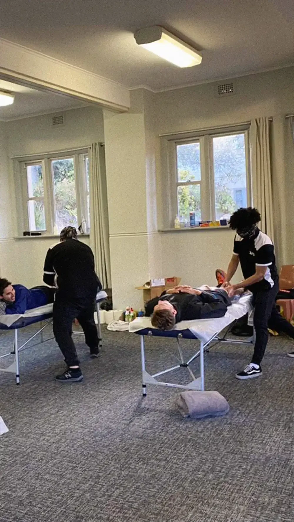 Two sports massage therapists in Liverpool treat clients on portable tables in a bright room.