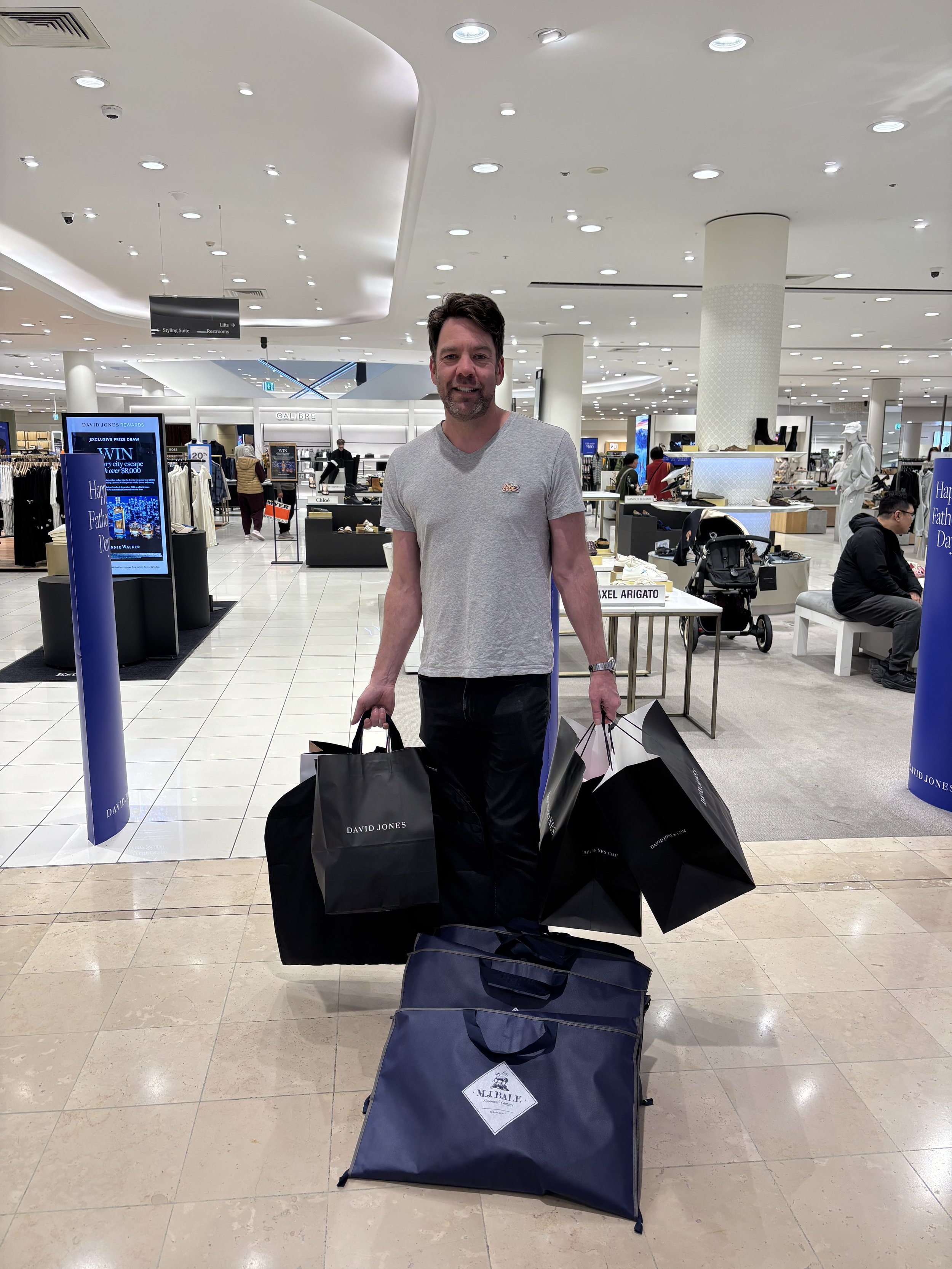 A man standing in a shopping mall, holding multiple shopping bags with 